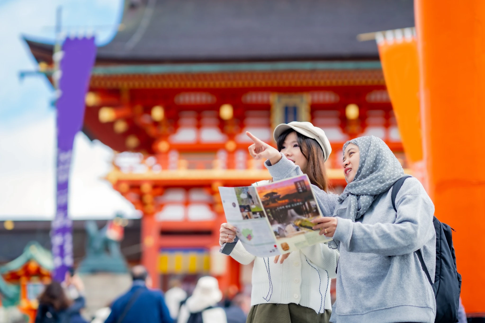 Travel, muslim, Two Asian female tourists of different religions friends visitor learning about history of fushimi inari shrine in travel book while walking through senbon torii path in Kyoto Japan..