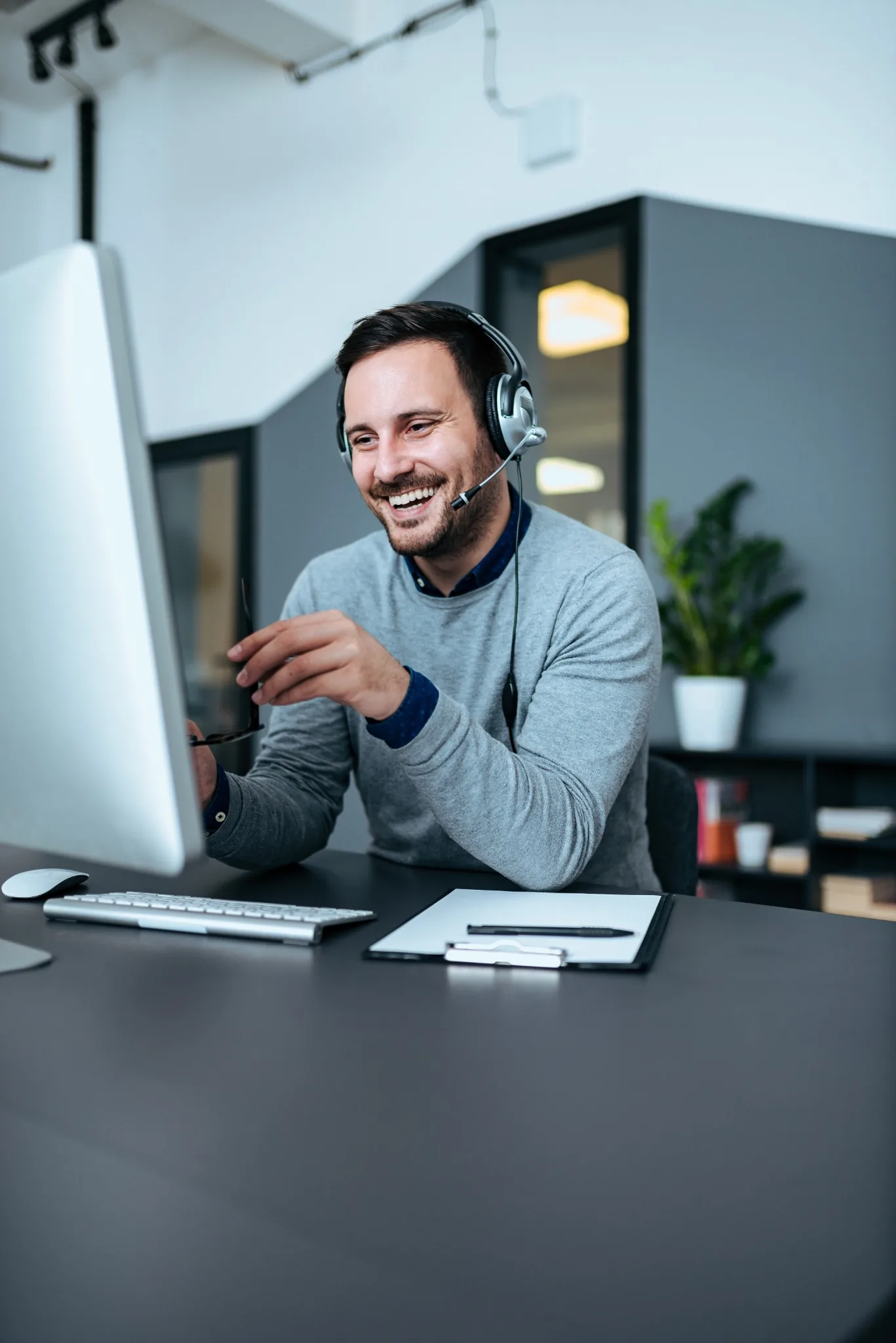 Man with headset on smiling at computer screen