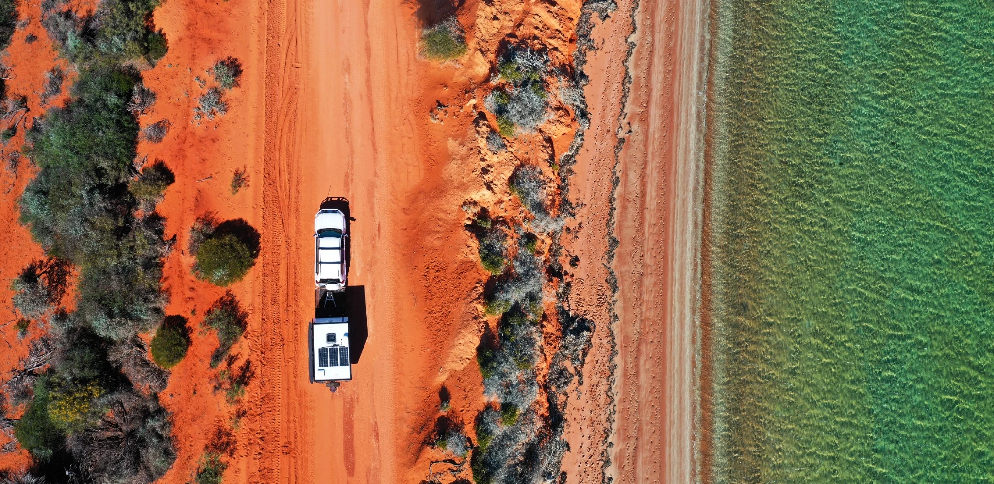 Panoramic aerial landscape view of vehicle towing a caravan on a dirt road along an exotic empty beach at Peron Peninsula in Shark Bay, Western Australia..