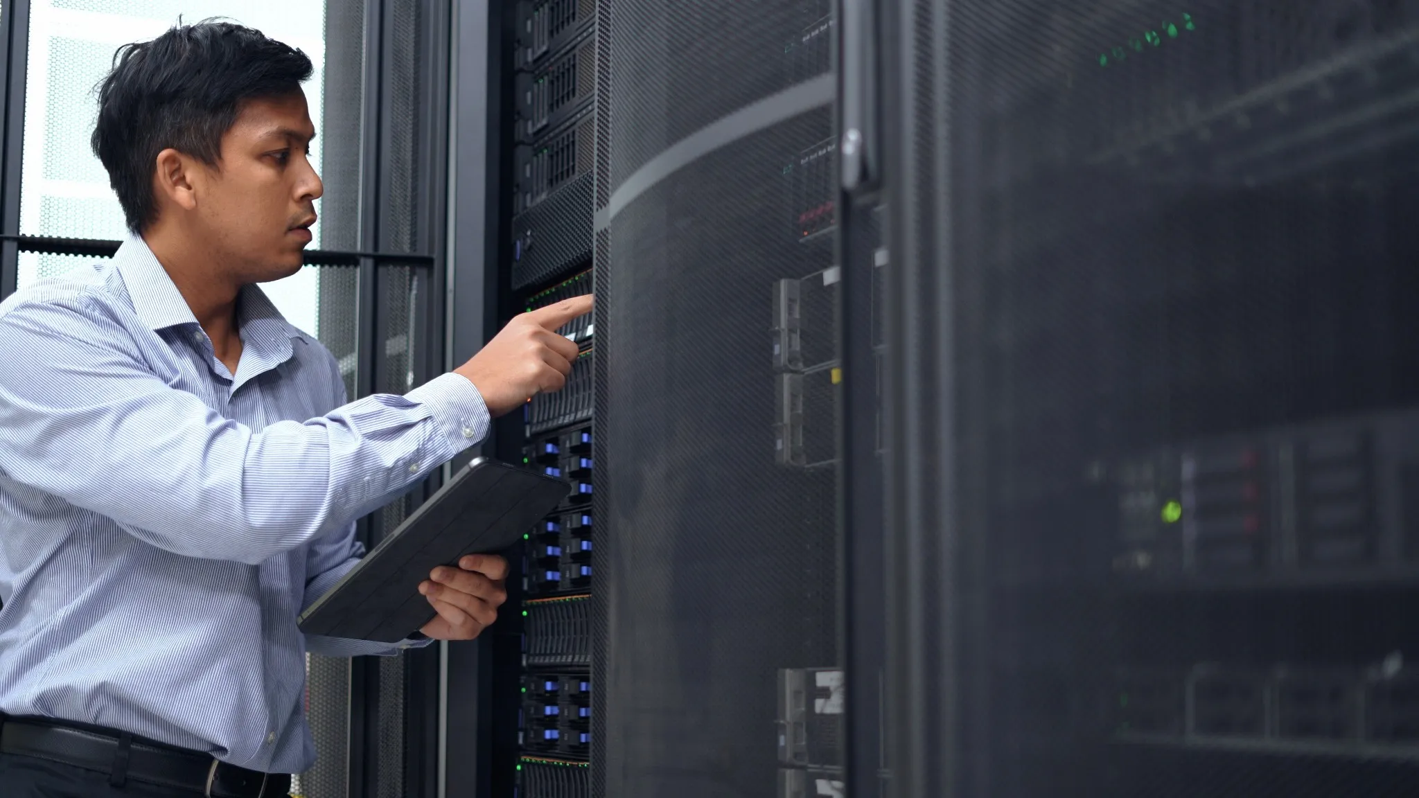 An IT professional in a blue shirt manages and monitors network servers in a data center, ensuring system stability and security.