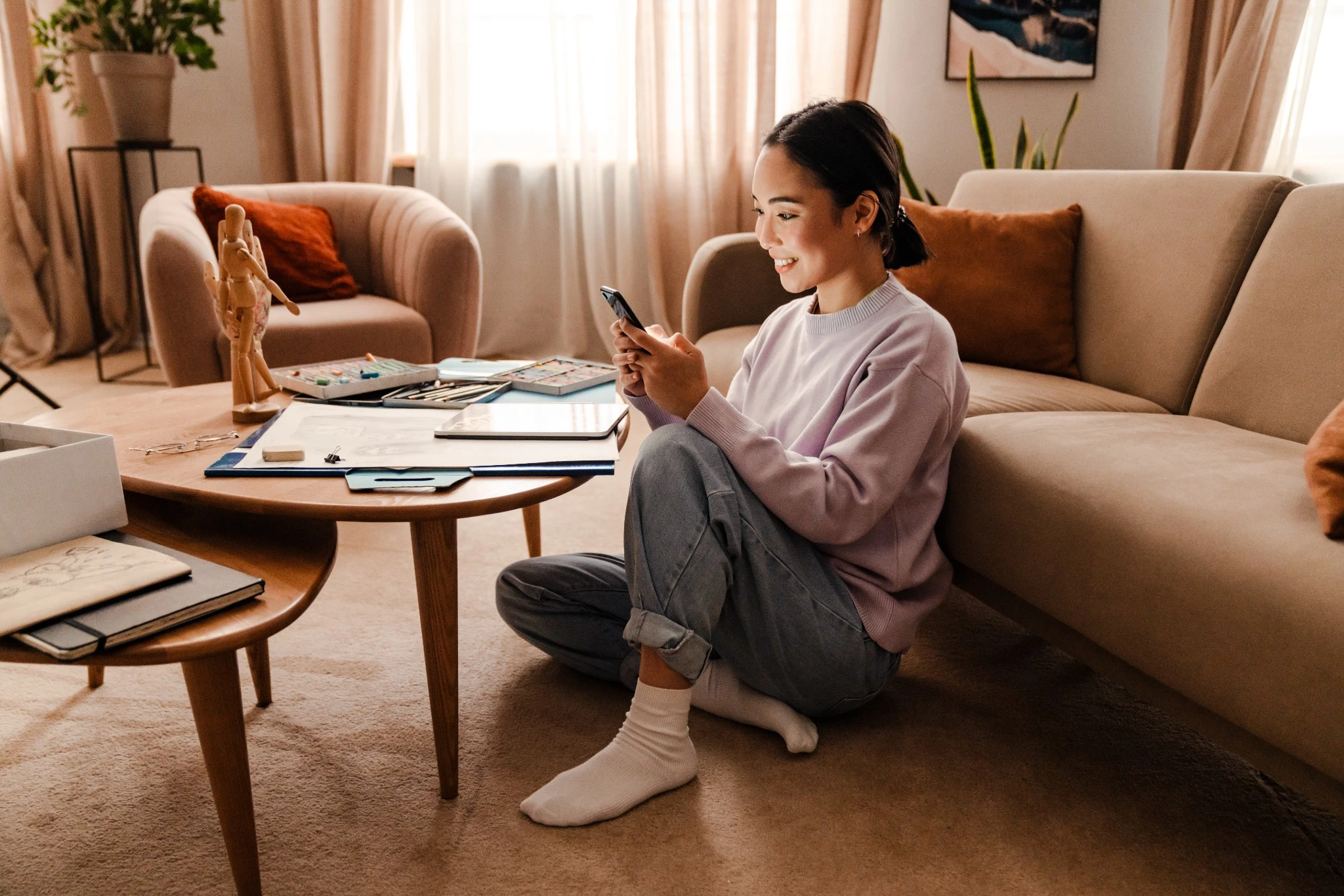 Cheerful asian woman using smart phone while sitting in living room.