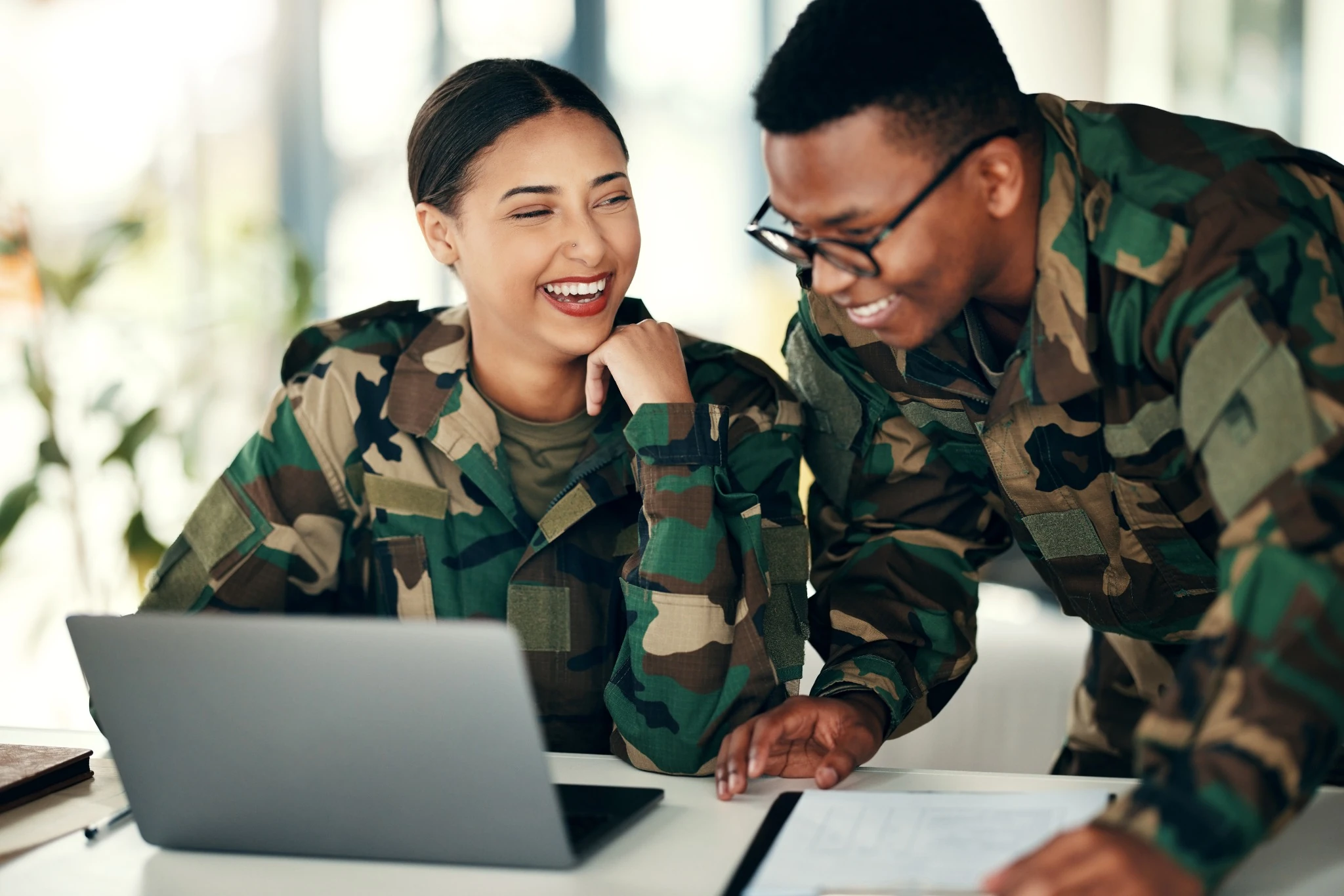 two military soldiers smiling and looking at laptop during training