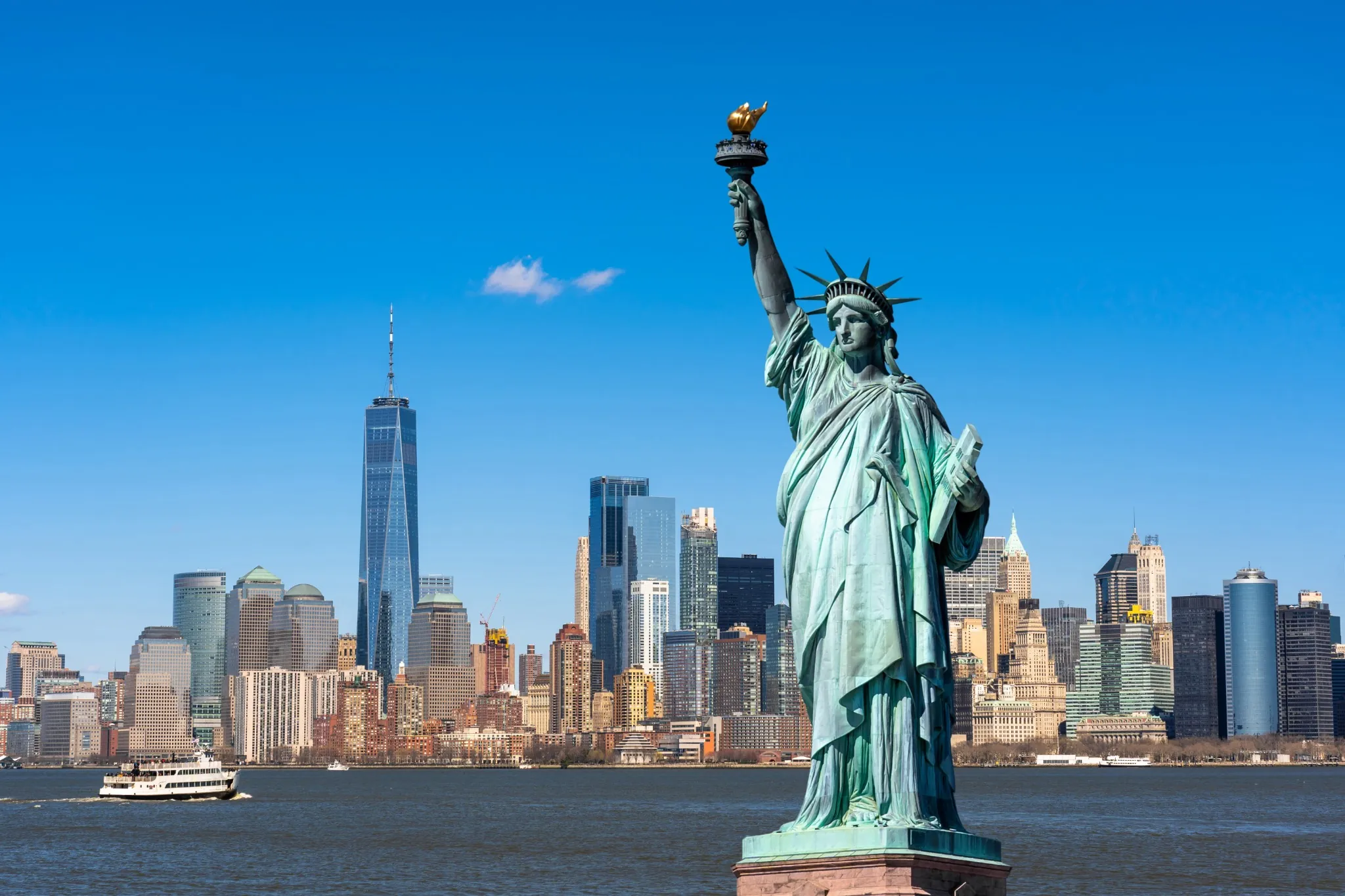 The Statue of Liberty on blue sky day with Manhattan NYC and boat in background