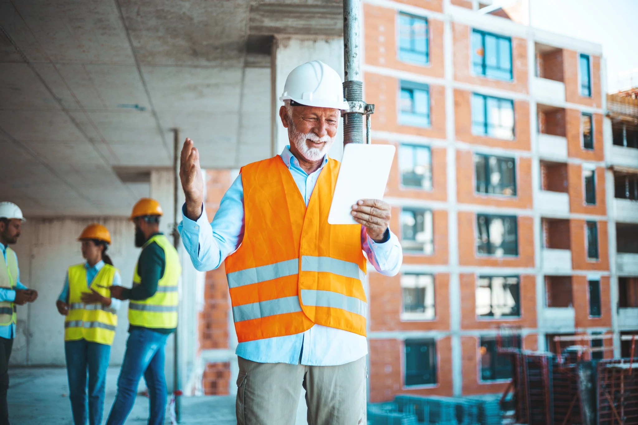 Mature man working on digital tablet at construction site. Mid adult manual worker with blue hardhat inspecting construction site while checking list on laptop..