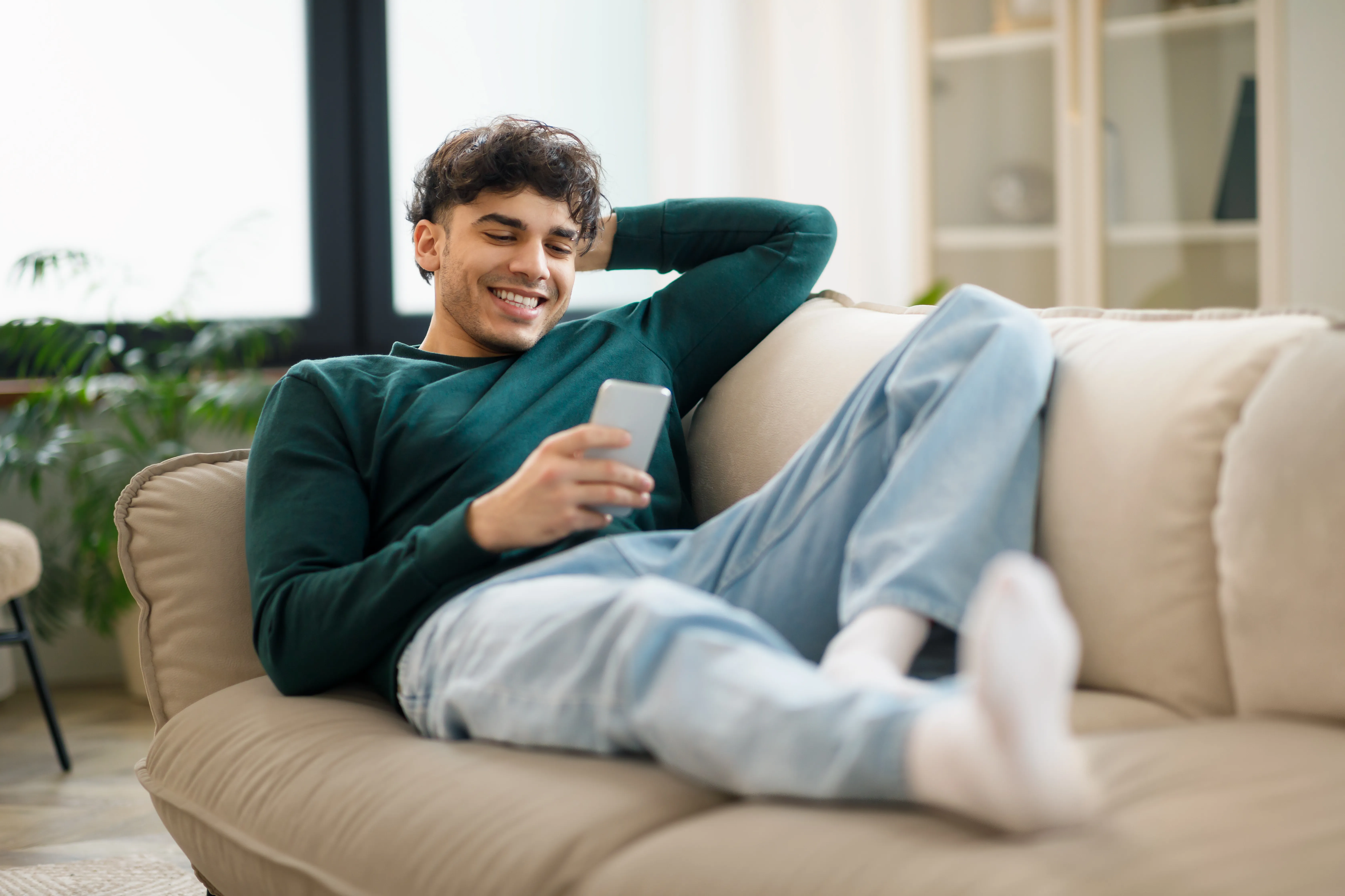 young man relaxing on the couch smiling at his phone