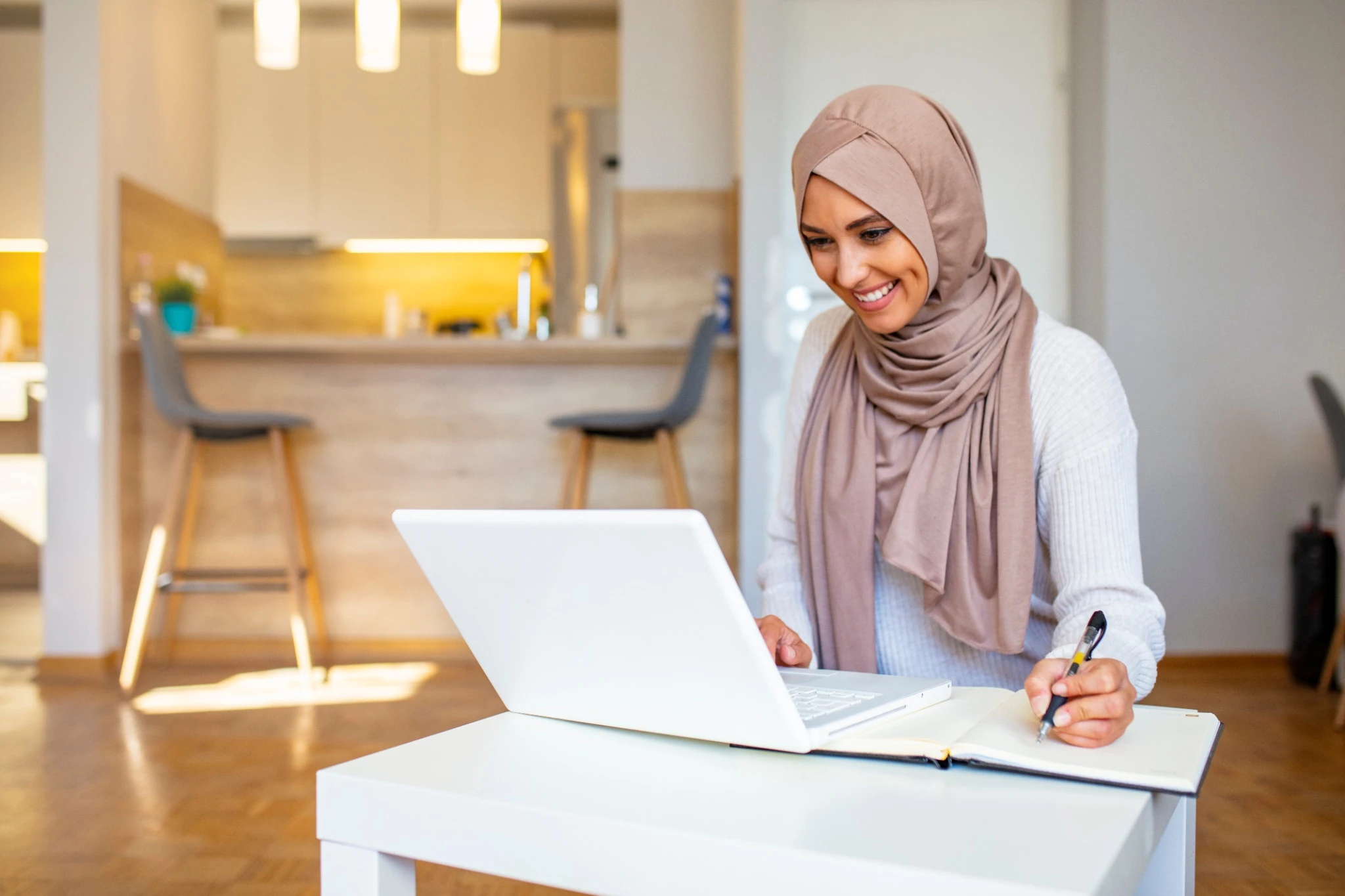 Pretty woman wearing hijab in front of laptop search and doing office work with different face expression isolated in home background - office, business, finance and work station concept.