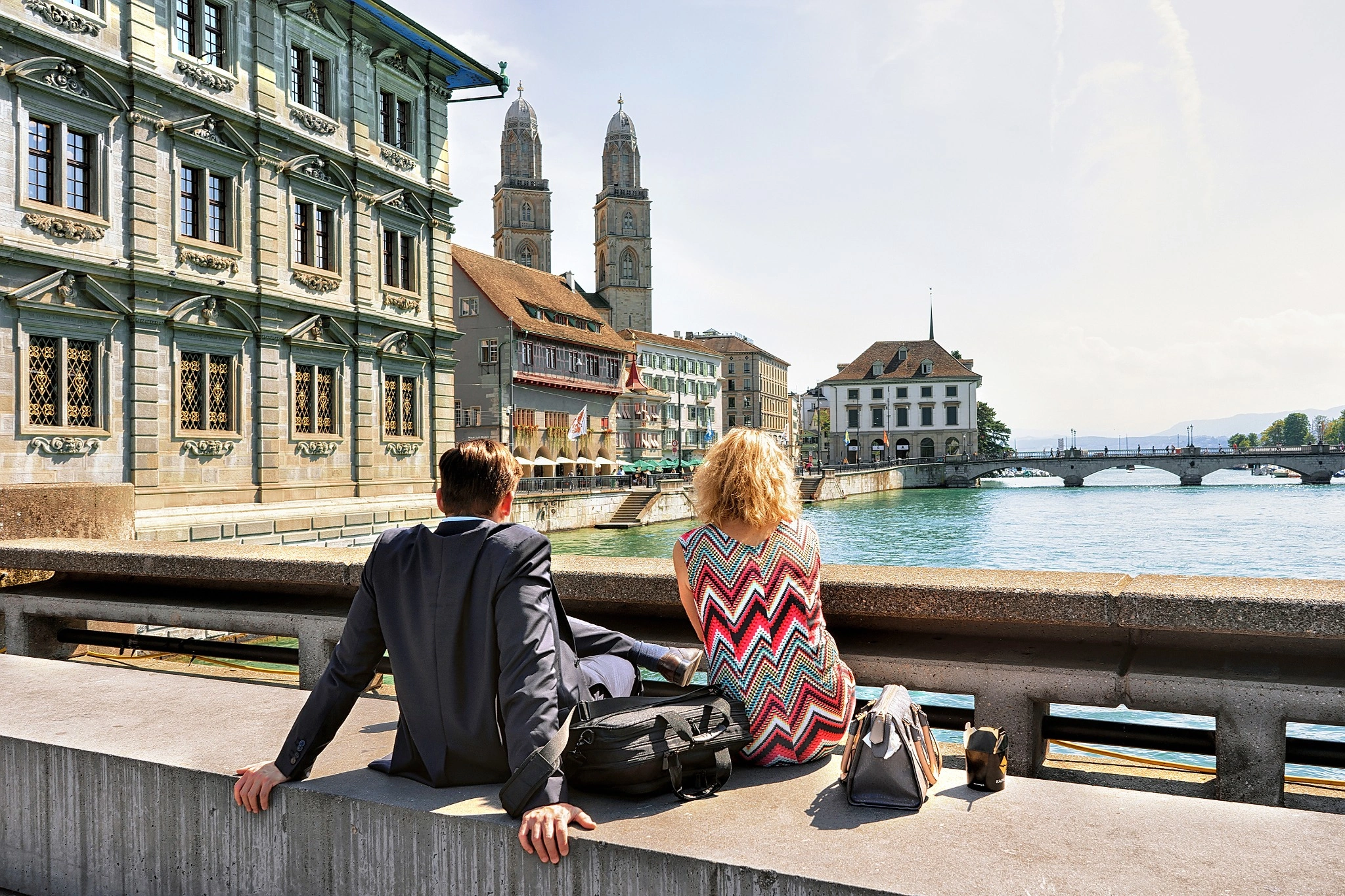 Romantic couple sitting at Limmat River Quay and looking at Grossmunster Church in Zurich, Switzerland.