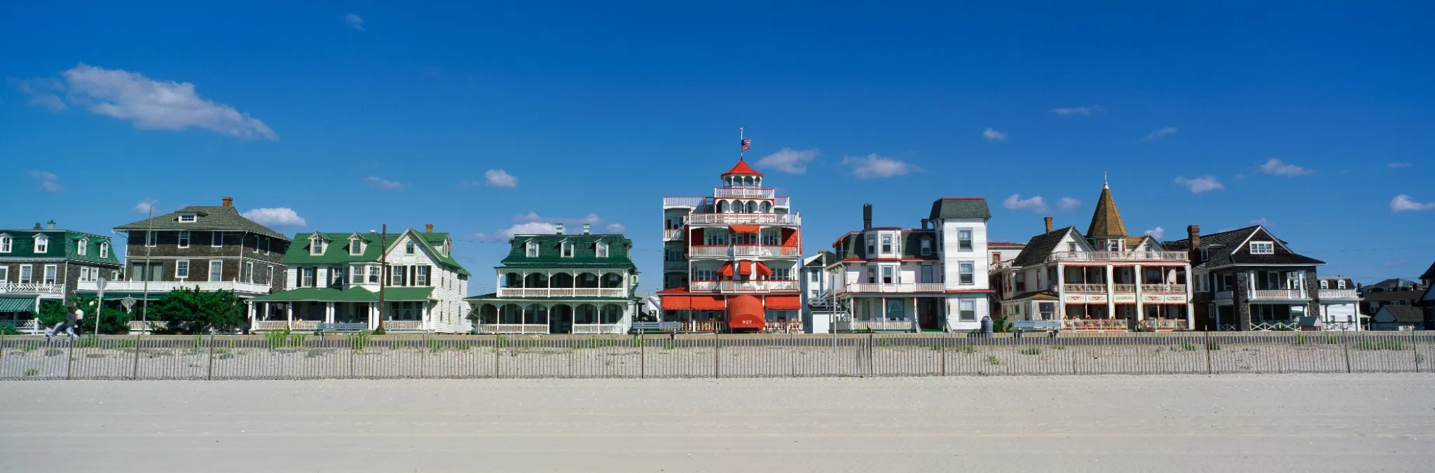 These are Victorian style homes overlooking the beach in Cape May. There is wooden fence separating the beach and the houses. 