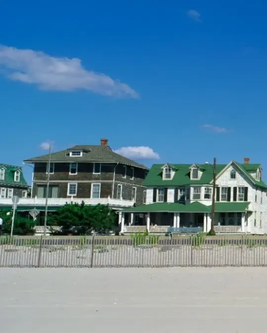 These are Victorian style homes overlooking the beach in Cape May. There is wooden fence separating the beach and the houses. 