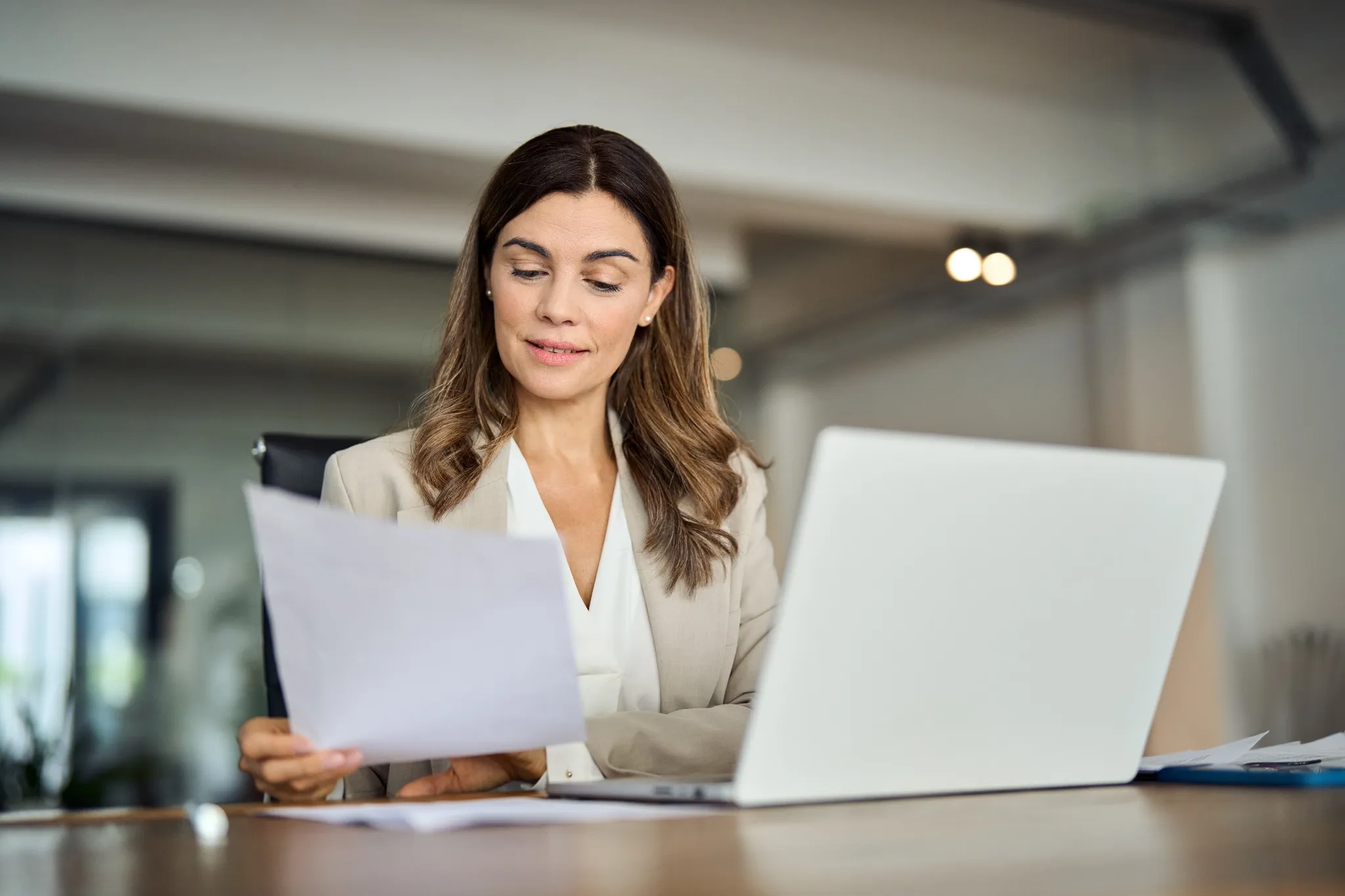 Woman at work looking at laptop and paper