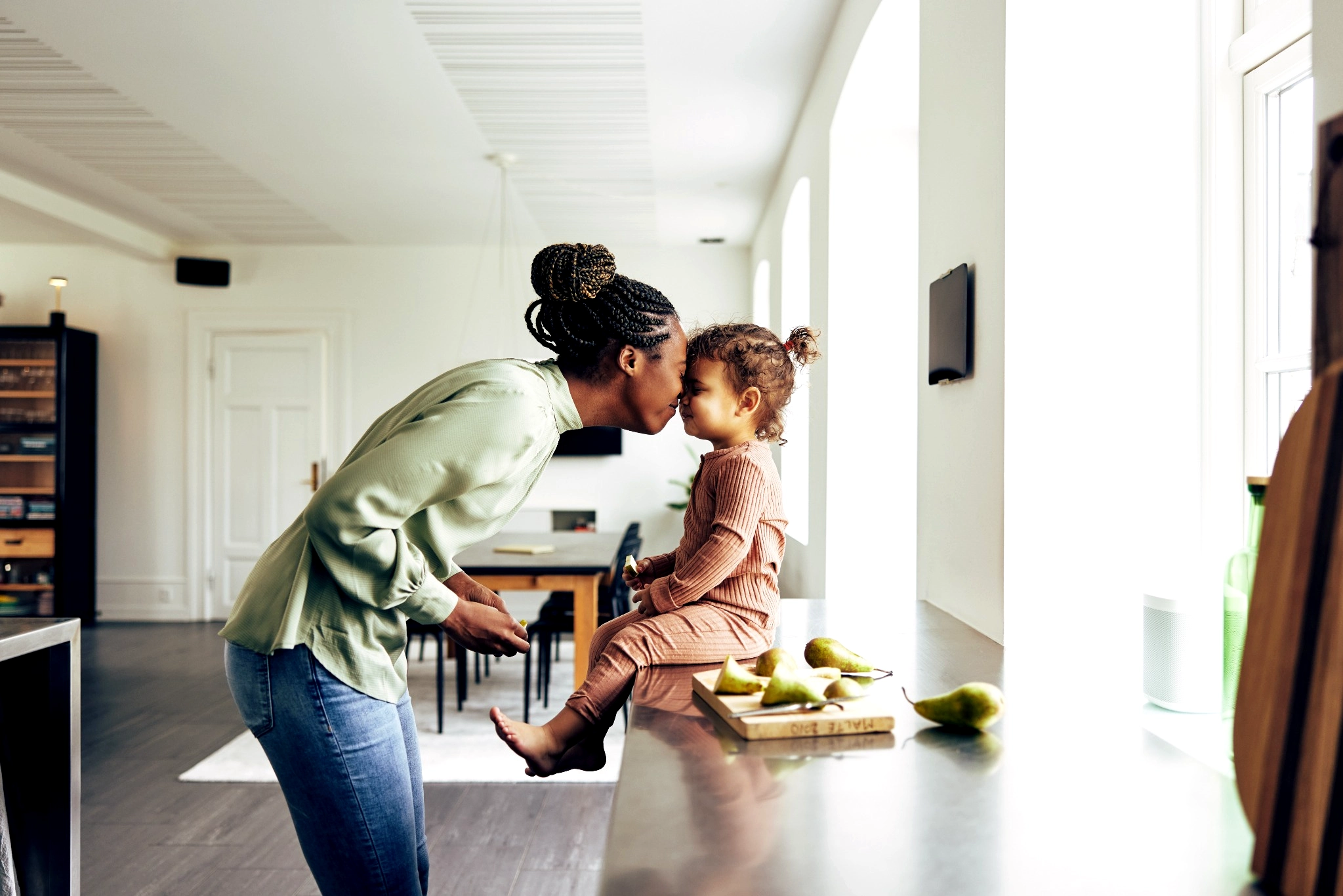 Woman nuzzling toddler girl sitting on the counter preparing a snack