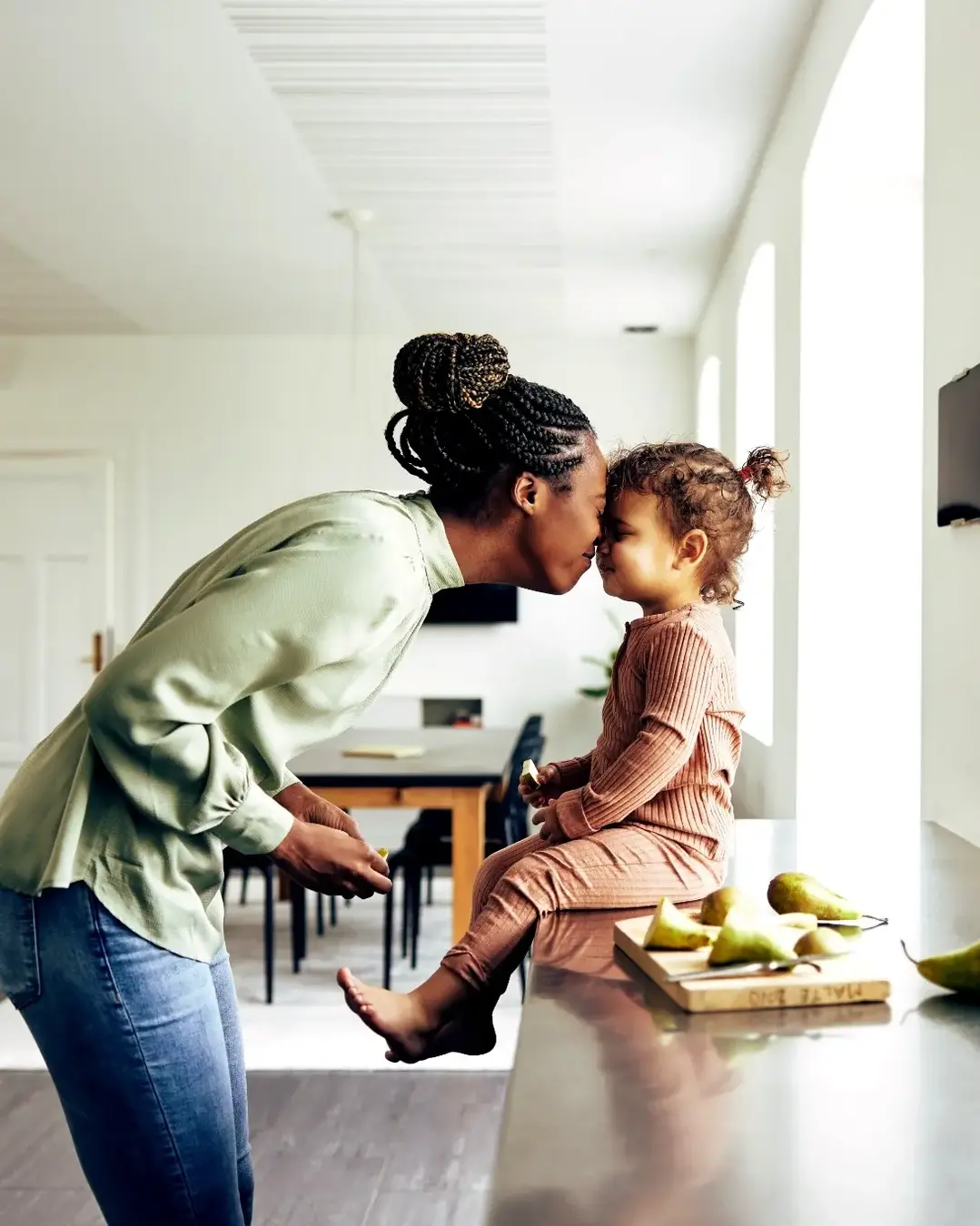 Woman nuzzling toddler girl sitting on the counter preparing a snack