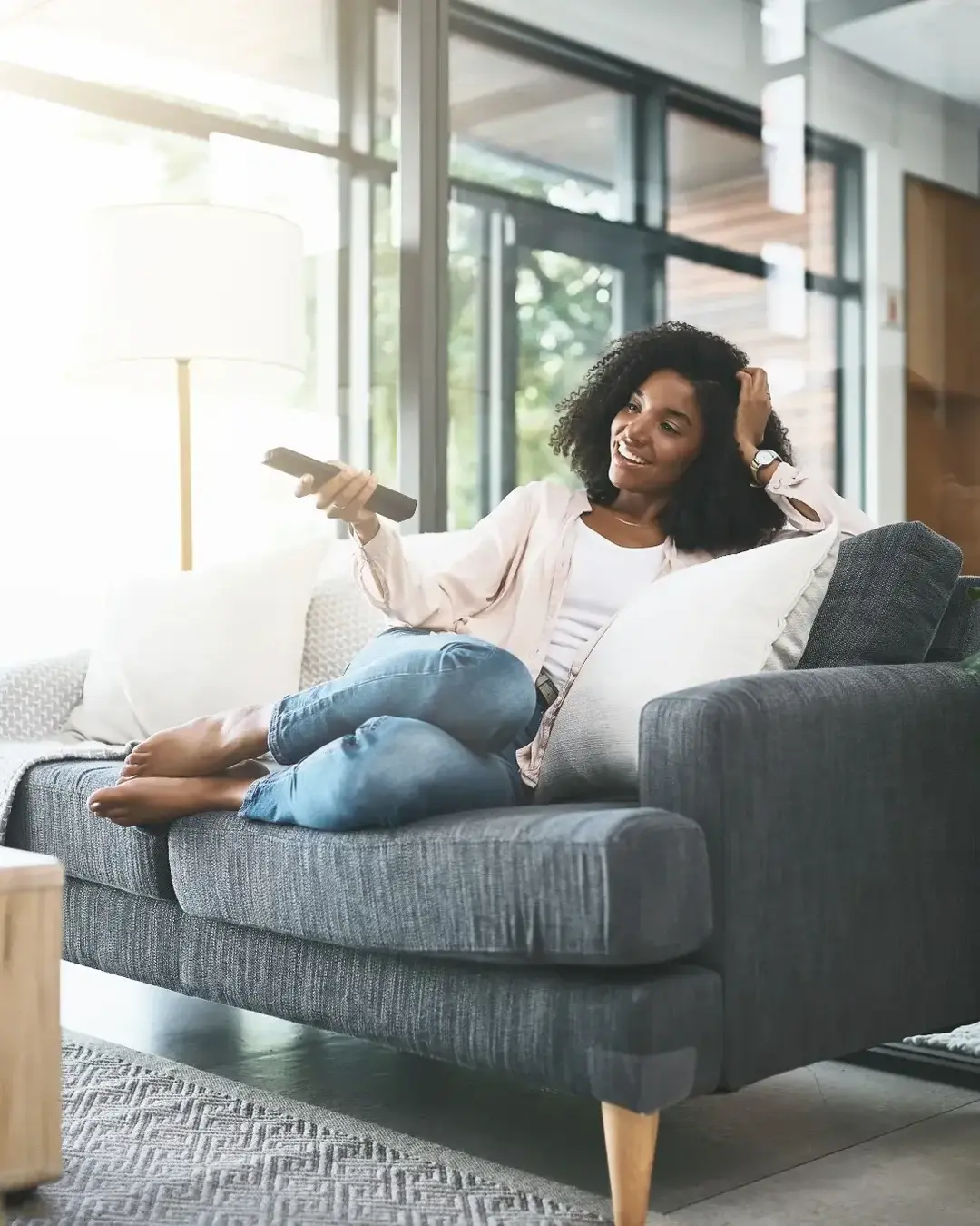 Black woman laying on couch with remote relaxing at home