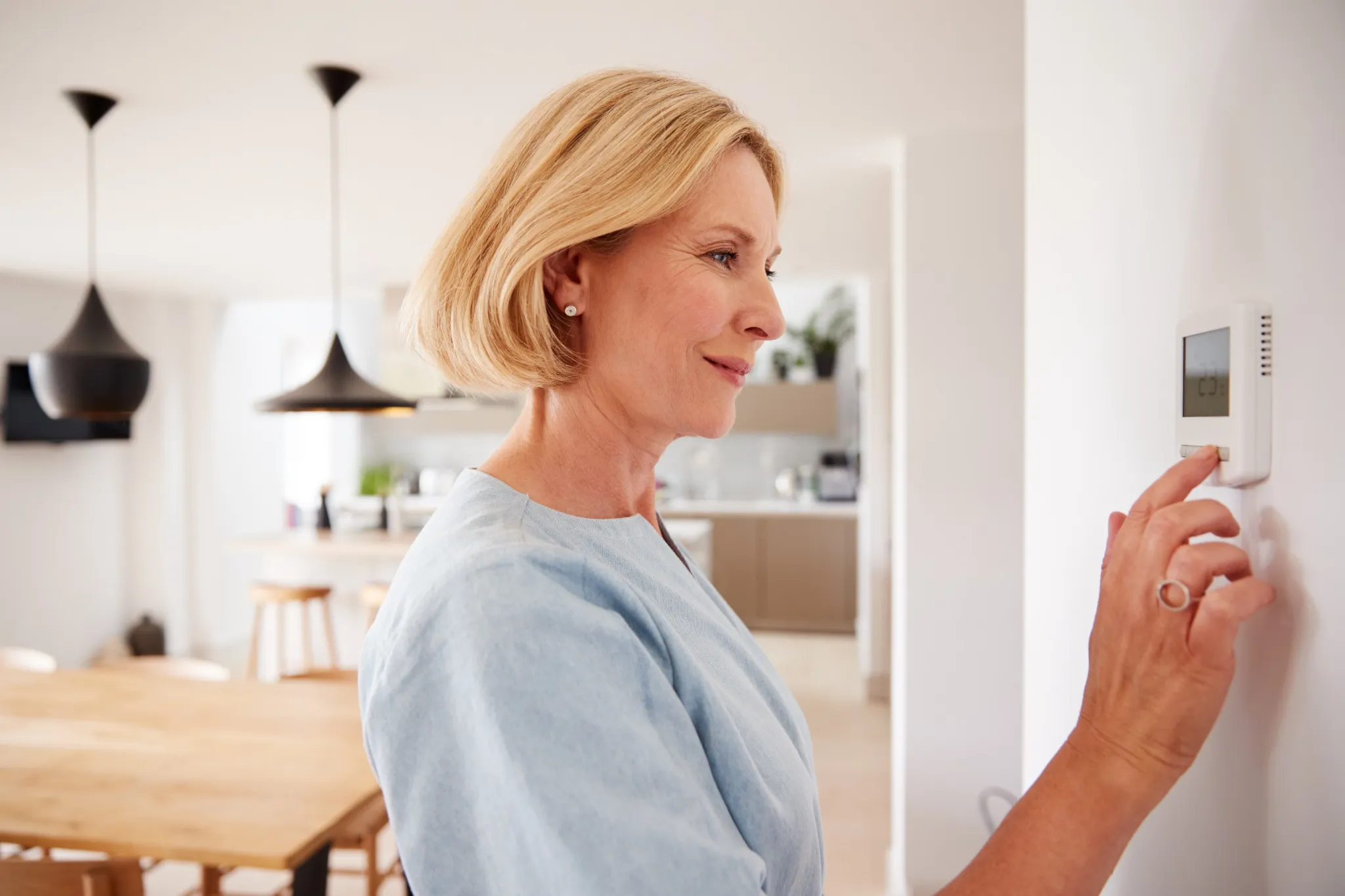 Close Up Of Mature Woman Adjusting Central Heating Temperature At Home On Thermostat