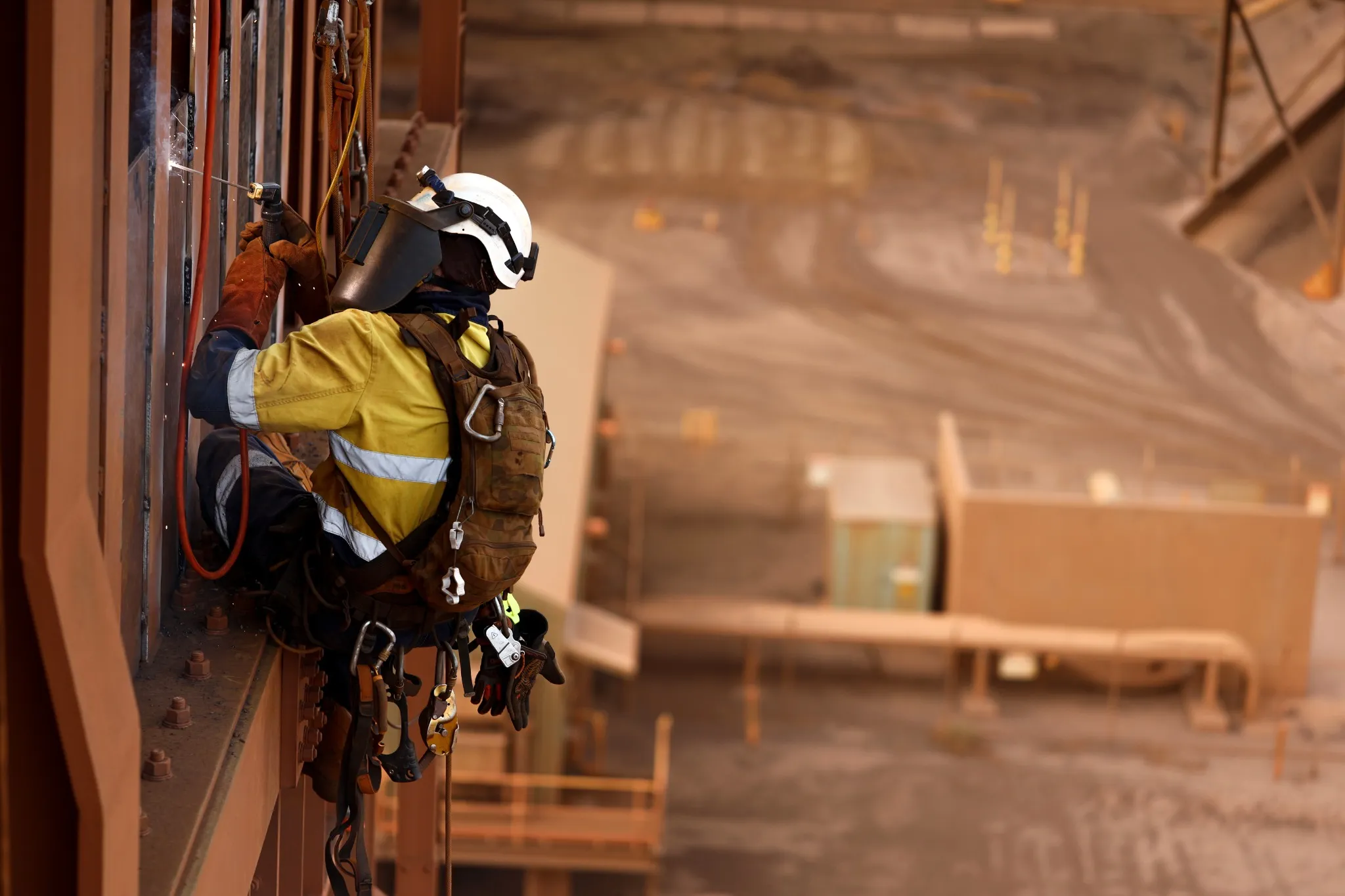Close up shoot of rope access stick welder wearing full body safety harness equipment, abseiling working at height conducting welding chute parent repairs on construction site Perth, Australia.