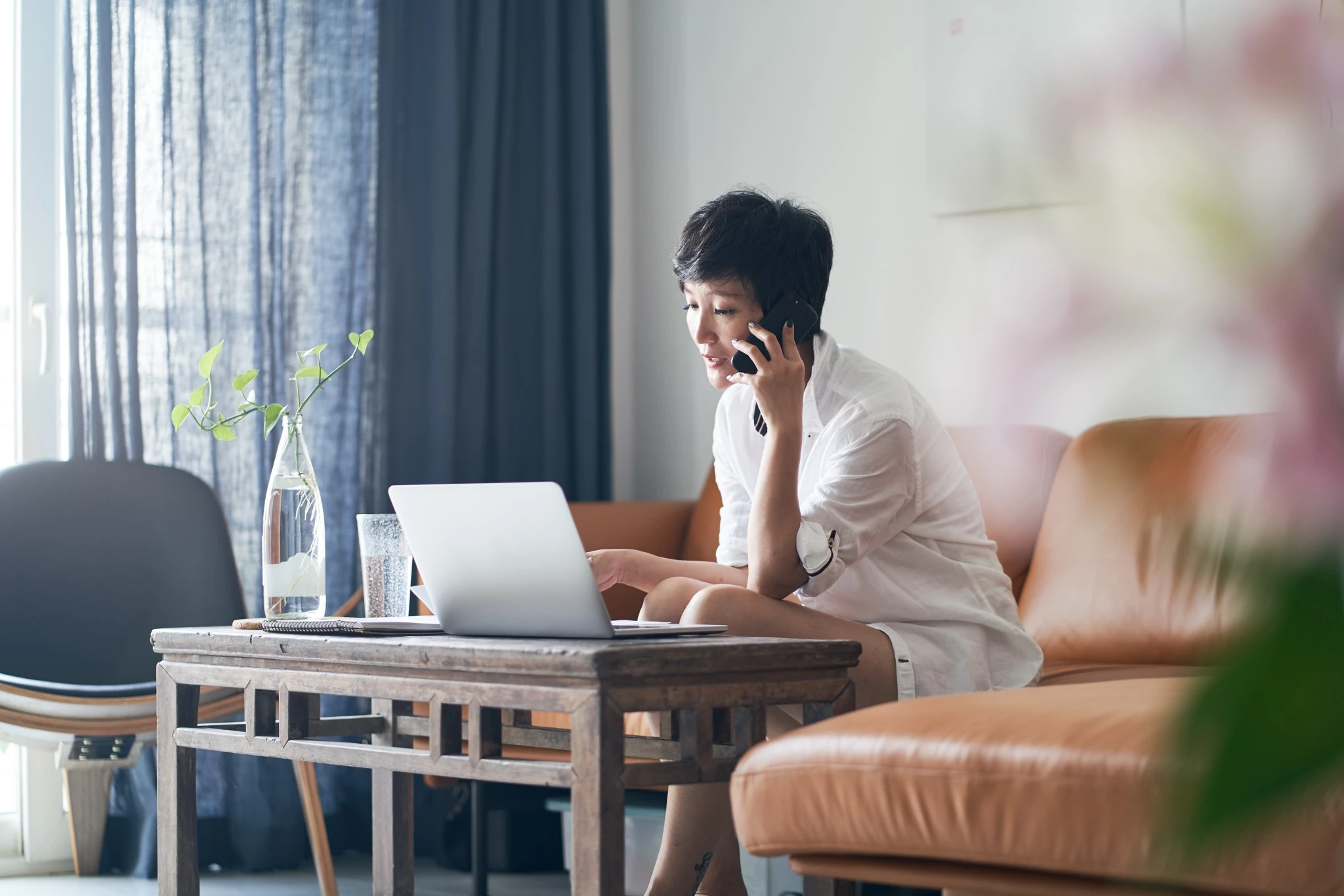 Asian self employed woman sitting on couch & working on laptop at home.