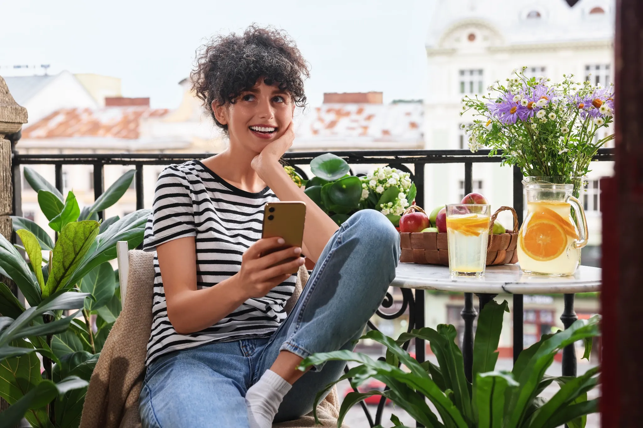Young woman using smartphone at table on balcony with houseplants