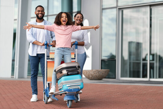 couple pushing luggage cart with young excited girl and luggage on it