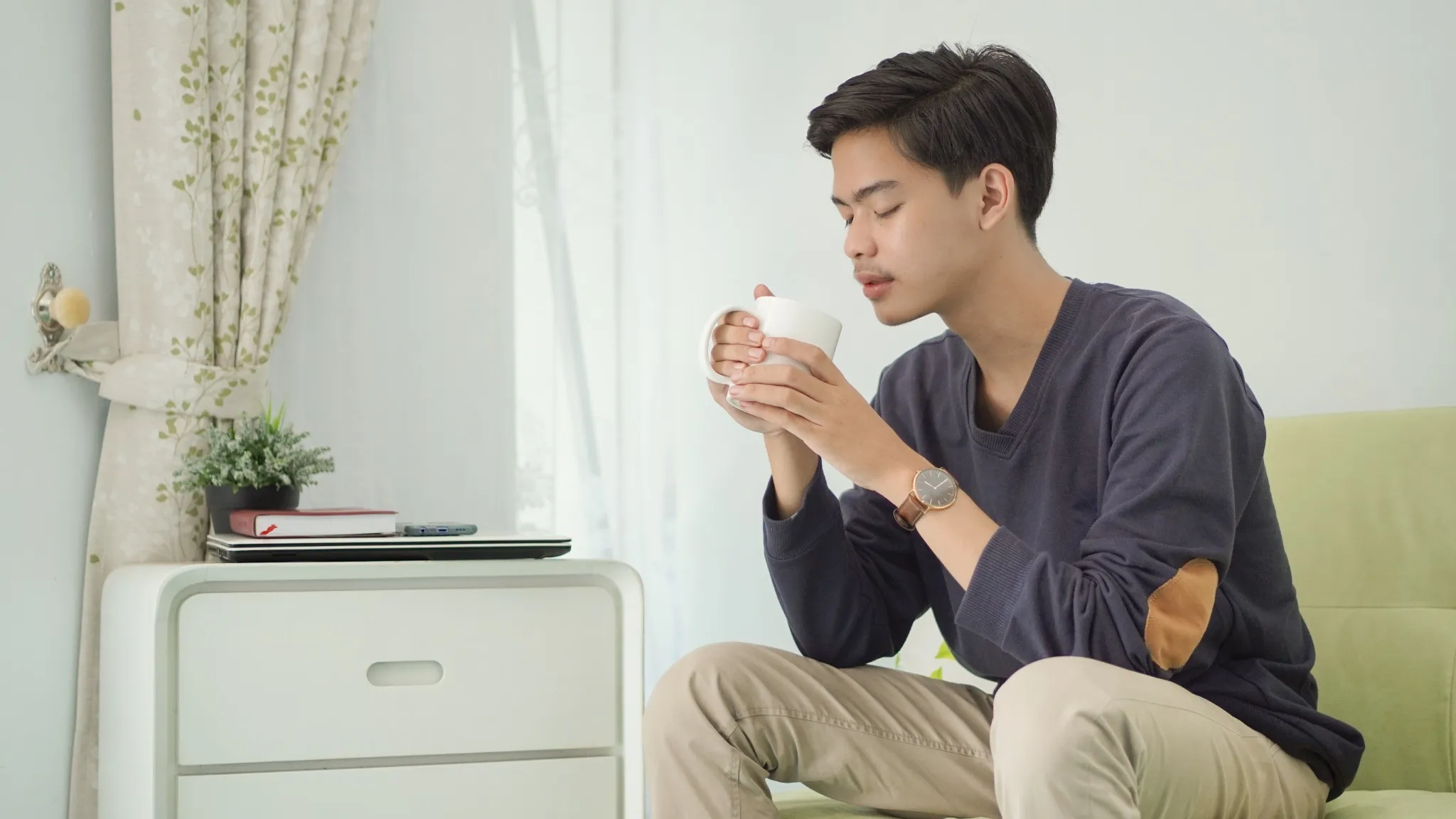 Man sitting on edge of couch drinking tea