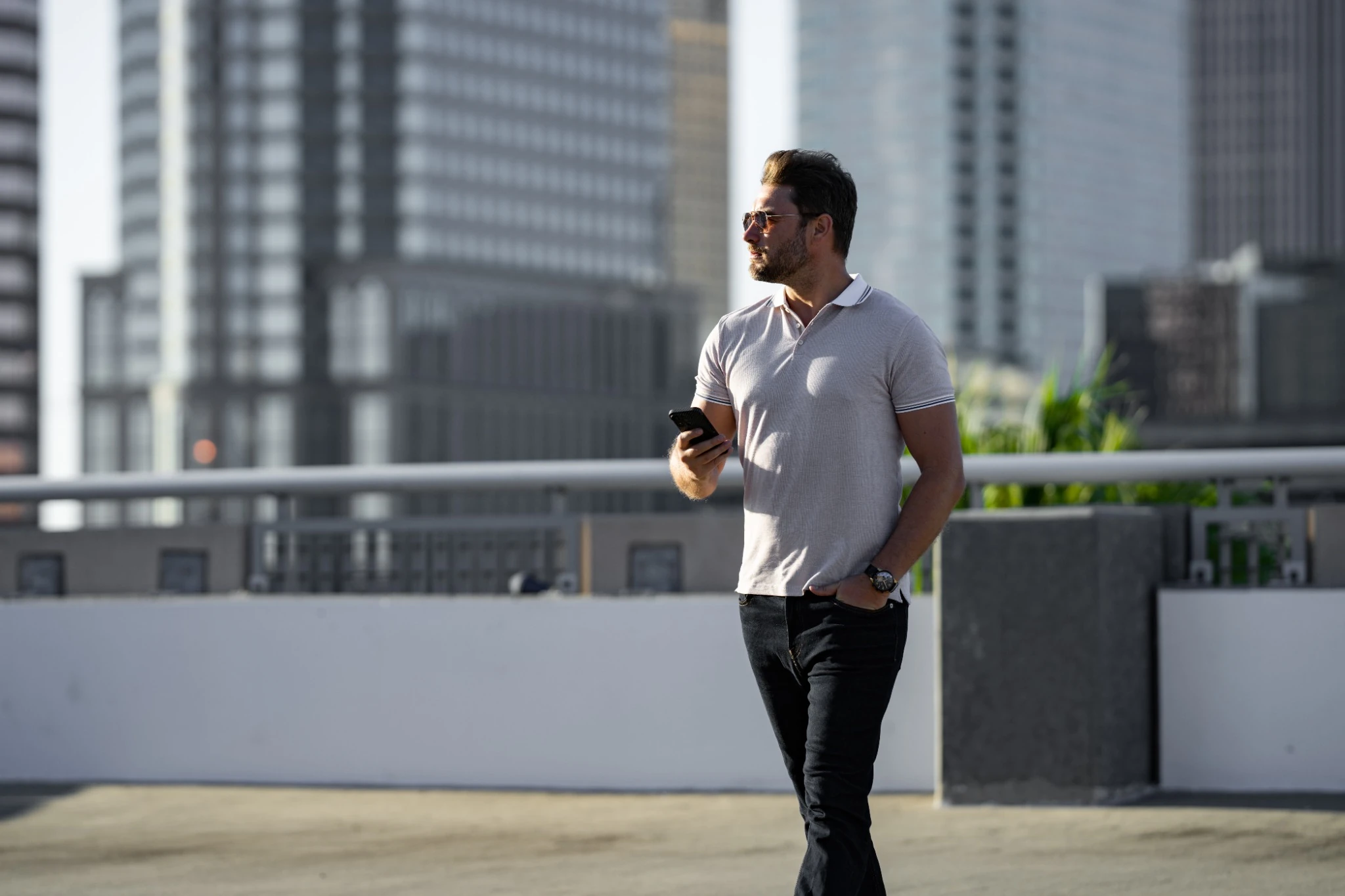 Portrait of handsome male model chatting on phone outdoor. Stylish man talking on phone dressed in polo. Fashion male posing on the street background. Urban style. Business phone conversation..