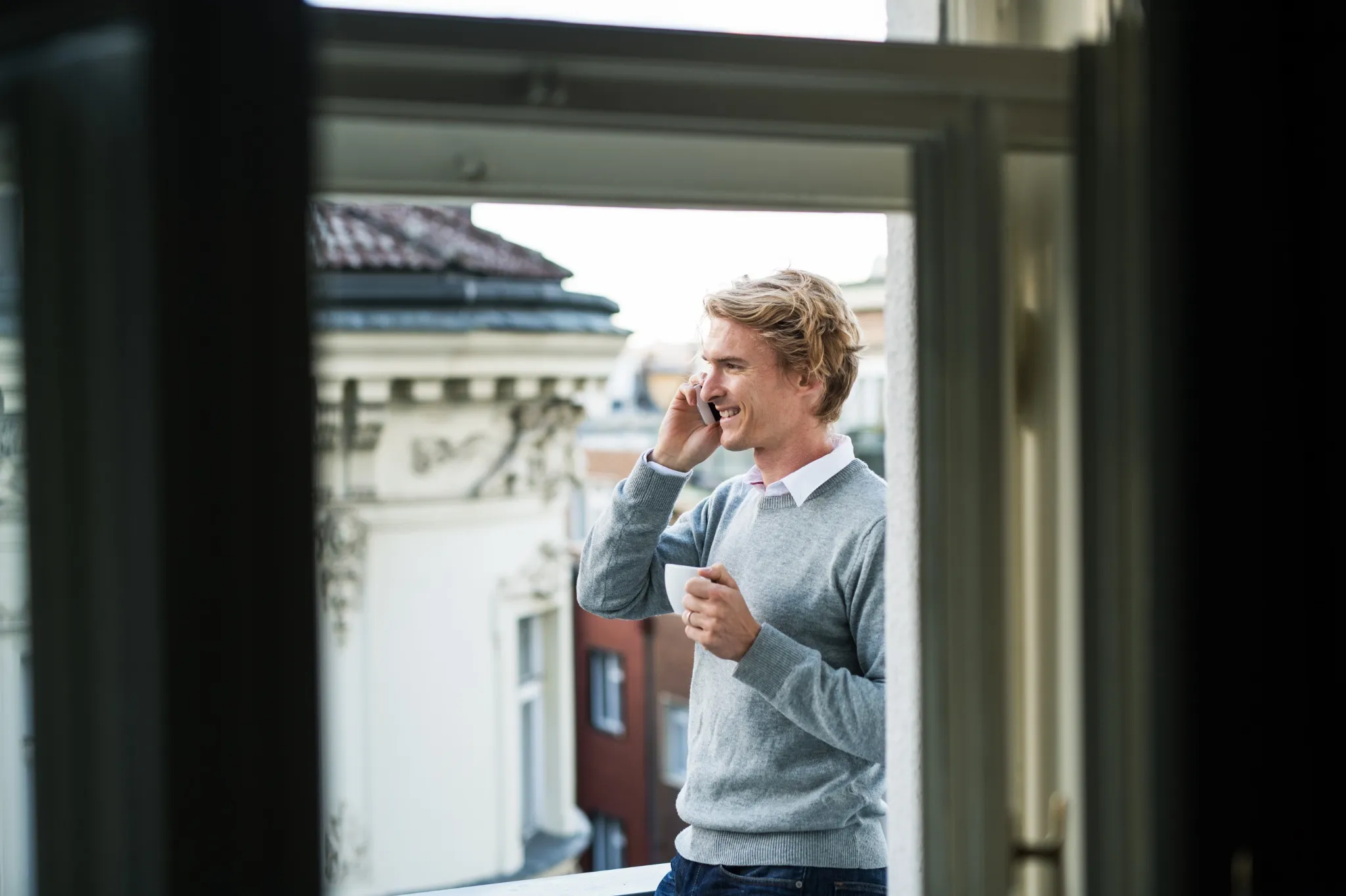 Young man with smartphone standing on a balcony in city, making a phone call.