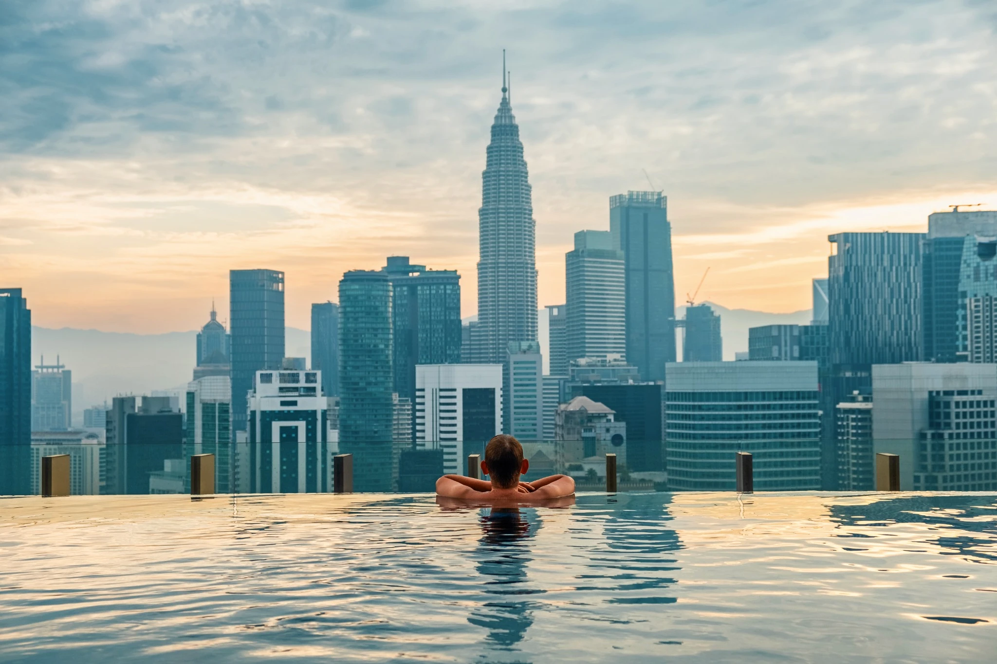 Man tourist relaxing in infinity roof top swimming pool at sunrise, Kuala Lumpur, Malaysia.