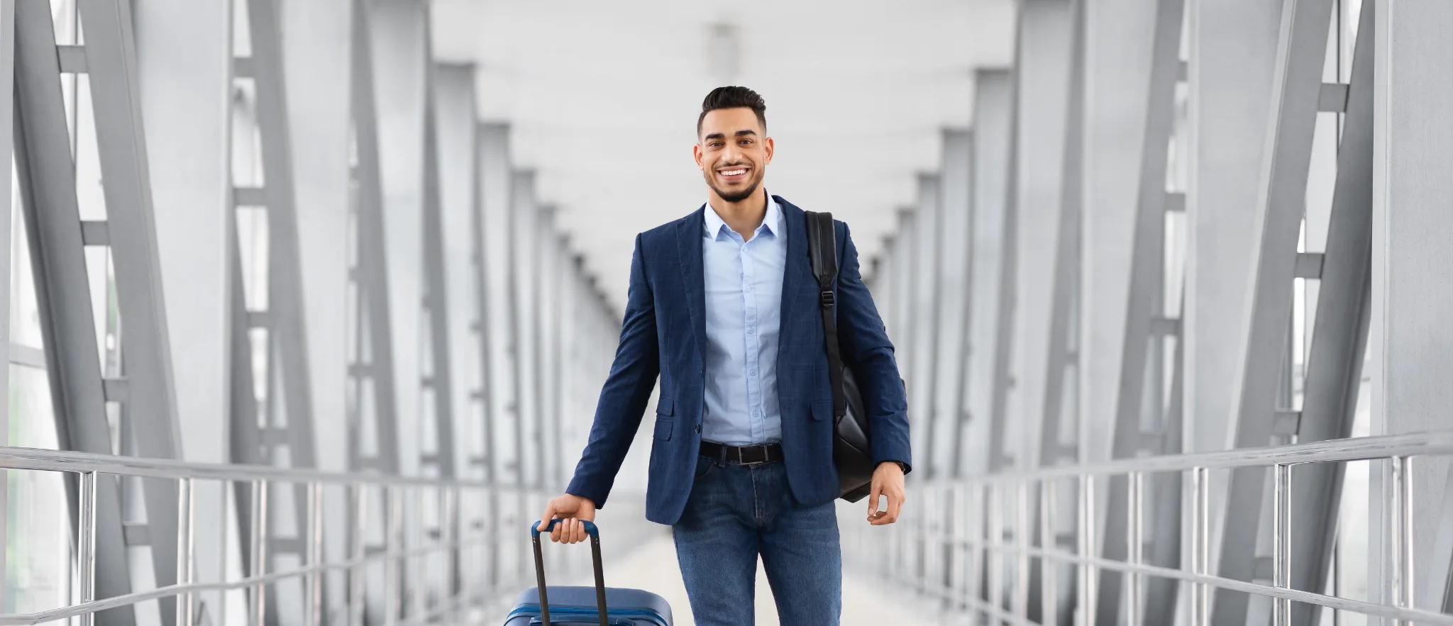 Man in business casual attire walking through airport pulling luggage
