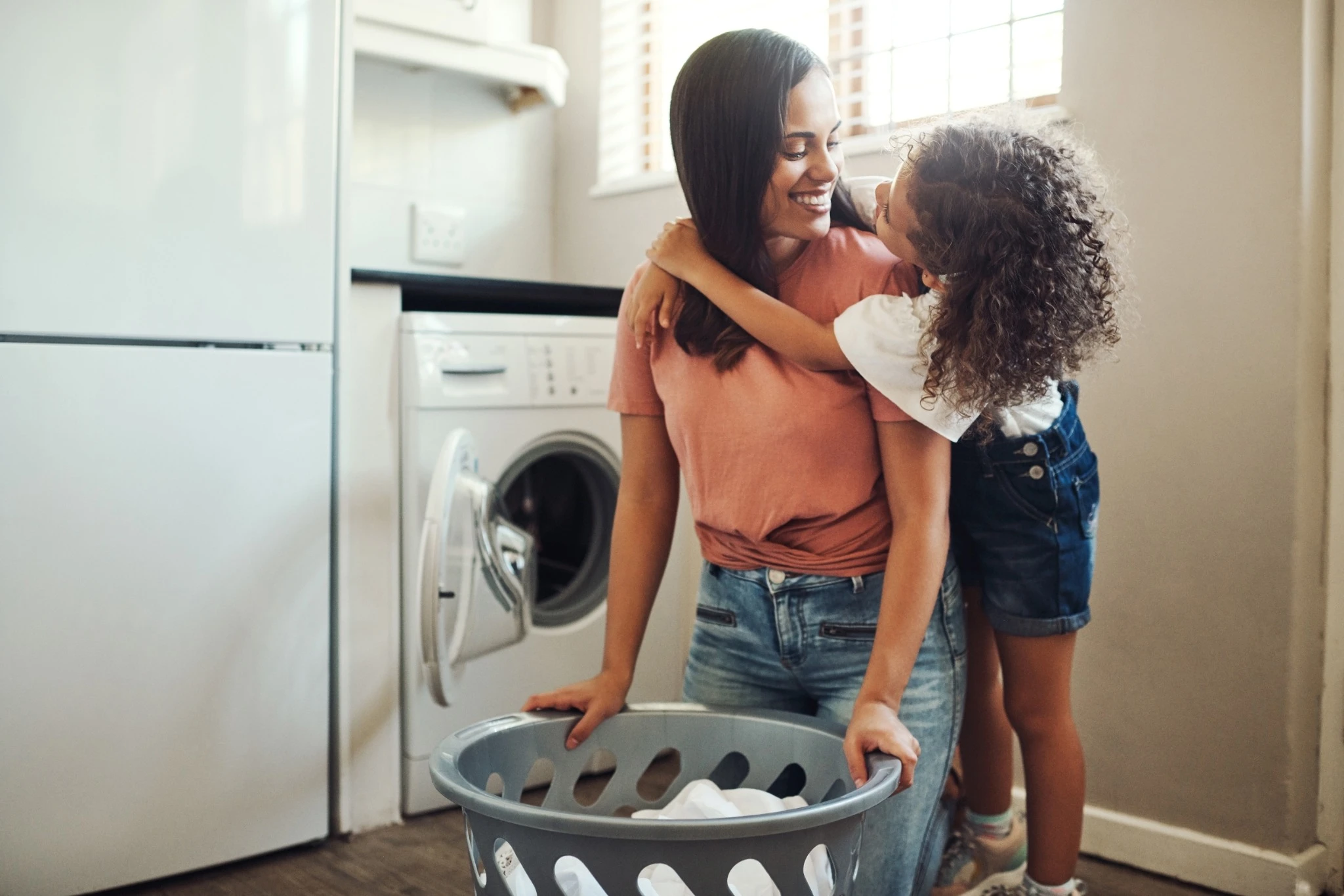 Have I told you I love you today. an adorable young girl hugging her mother while helping her with the laundry at home.