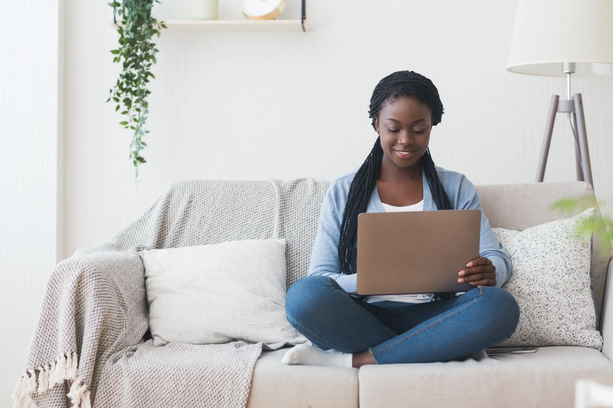 Black millennial woman working with laptop computer on sofa at home.