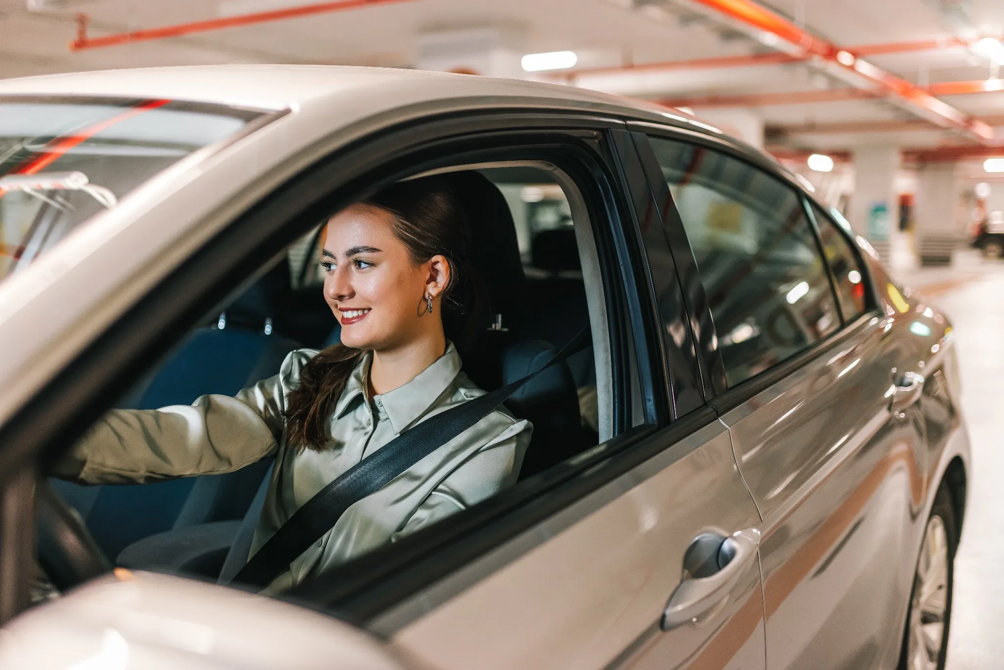 Young woman searching for parking spot in underground garage. Driving around in her car.