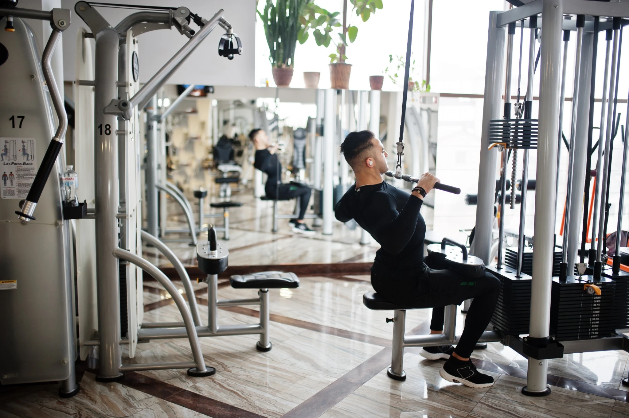 Muscular arab man training and doing workout on fitness machine in modern gym..