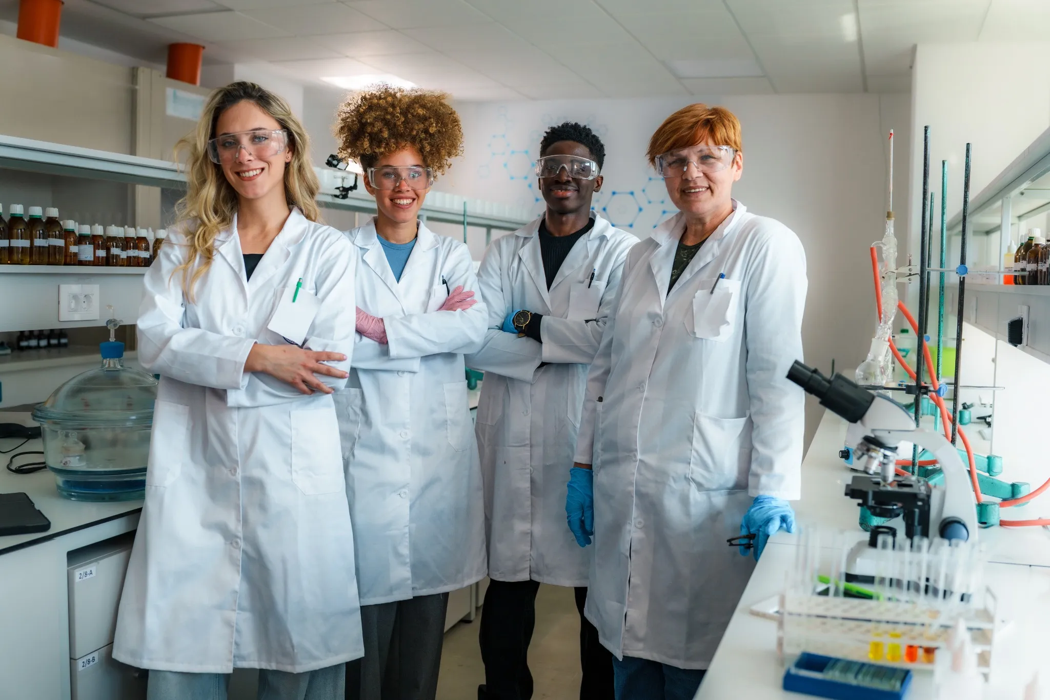 Four diverse scientists and their professor stand confidently in a brightly lit laboratory. Surrounded by scientific equipment and chemicals.