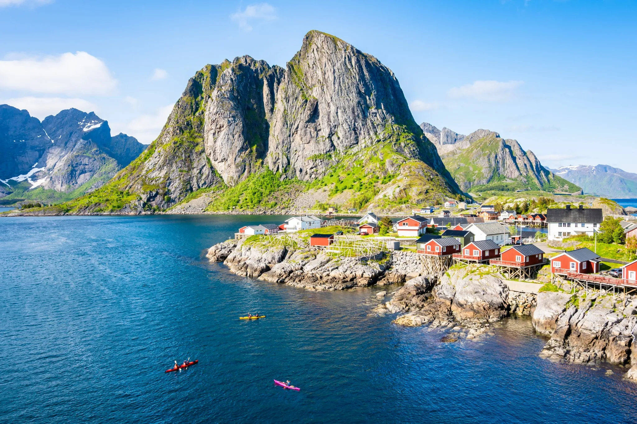 Colourful kayaks on sea, mountains and red traditional type houses used by fishermen's in Hamnoy village on Moskenesoy island in summer