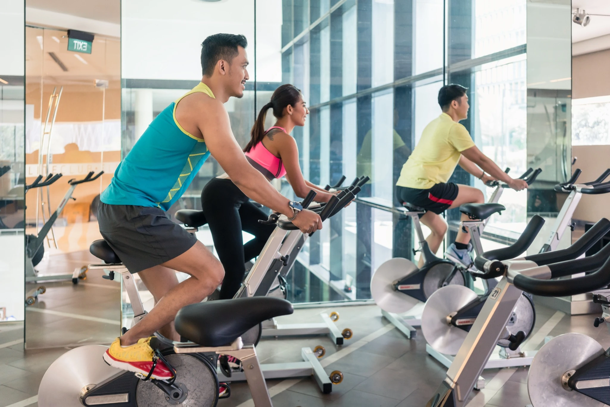handsome and confident young man smiling while pedaling during group class of HIIT indoor cycling in a modern fitness club.