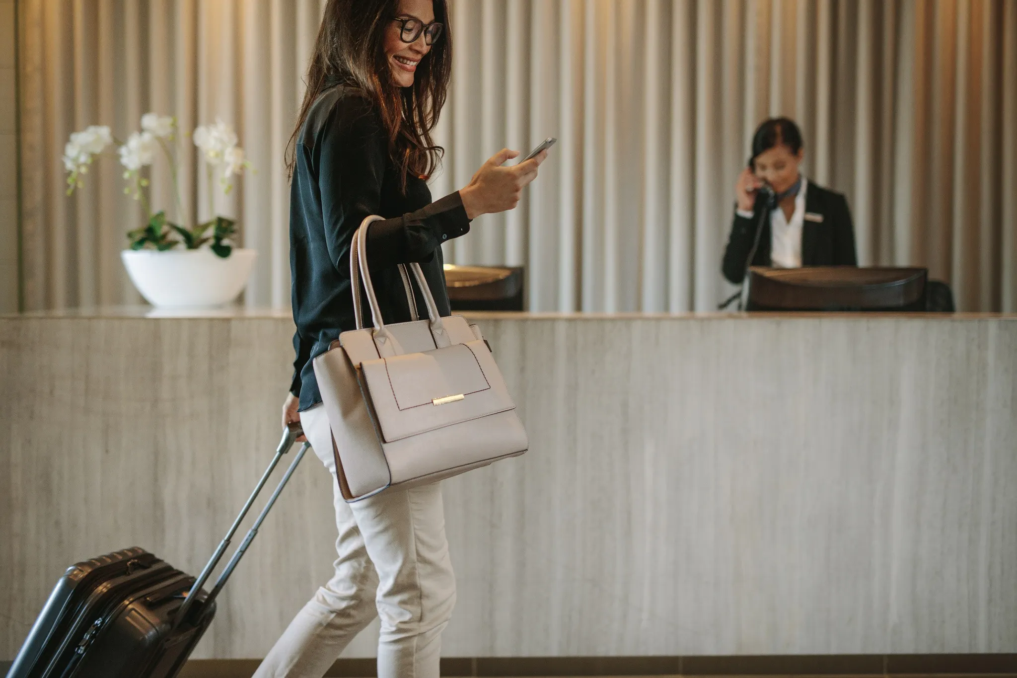Woman on phone pulling bag through hotel lobby