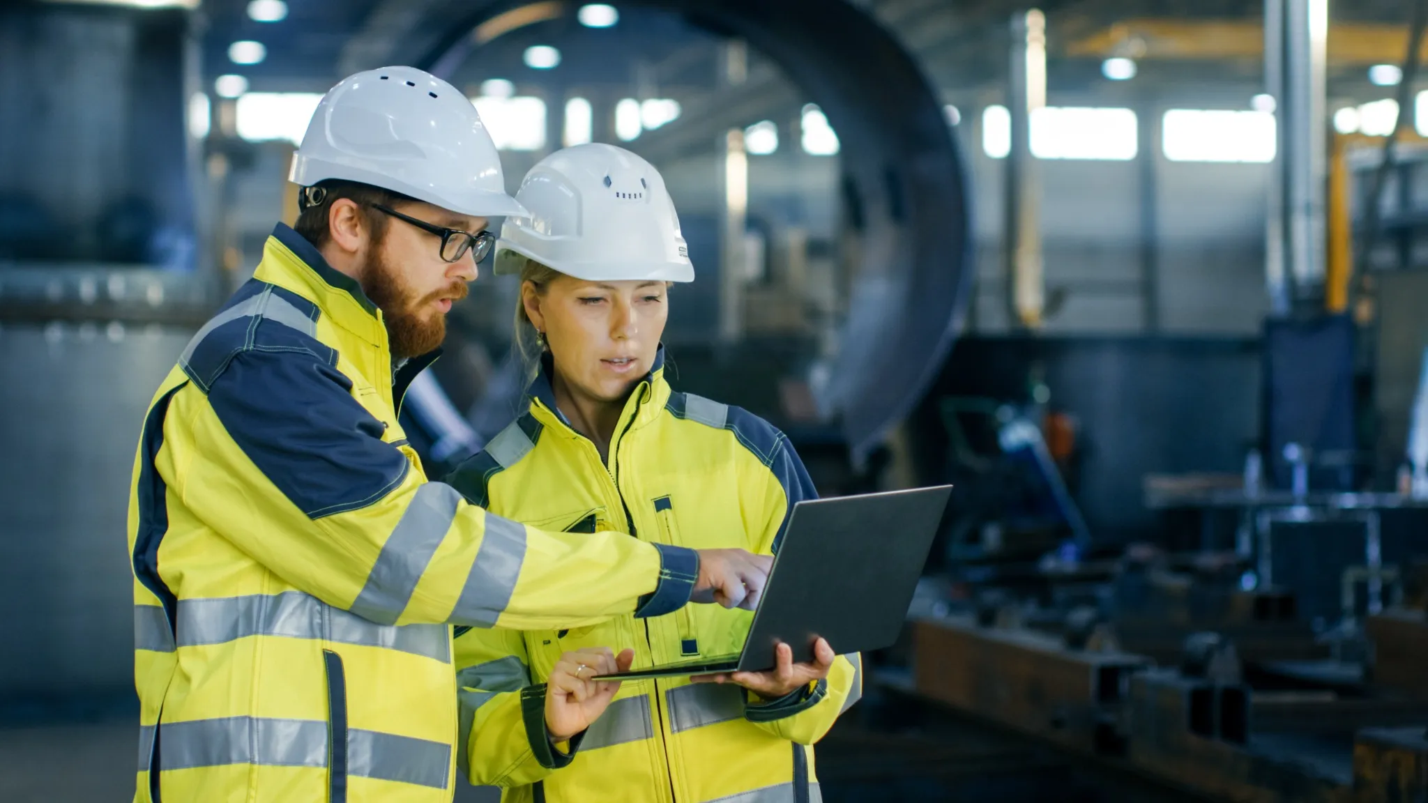 Two people look at a laptop with safety gear on