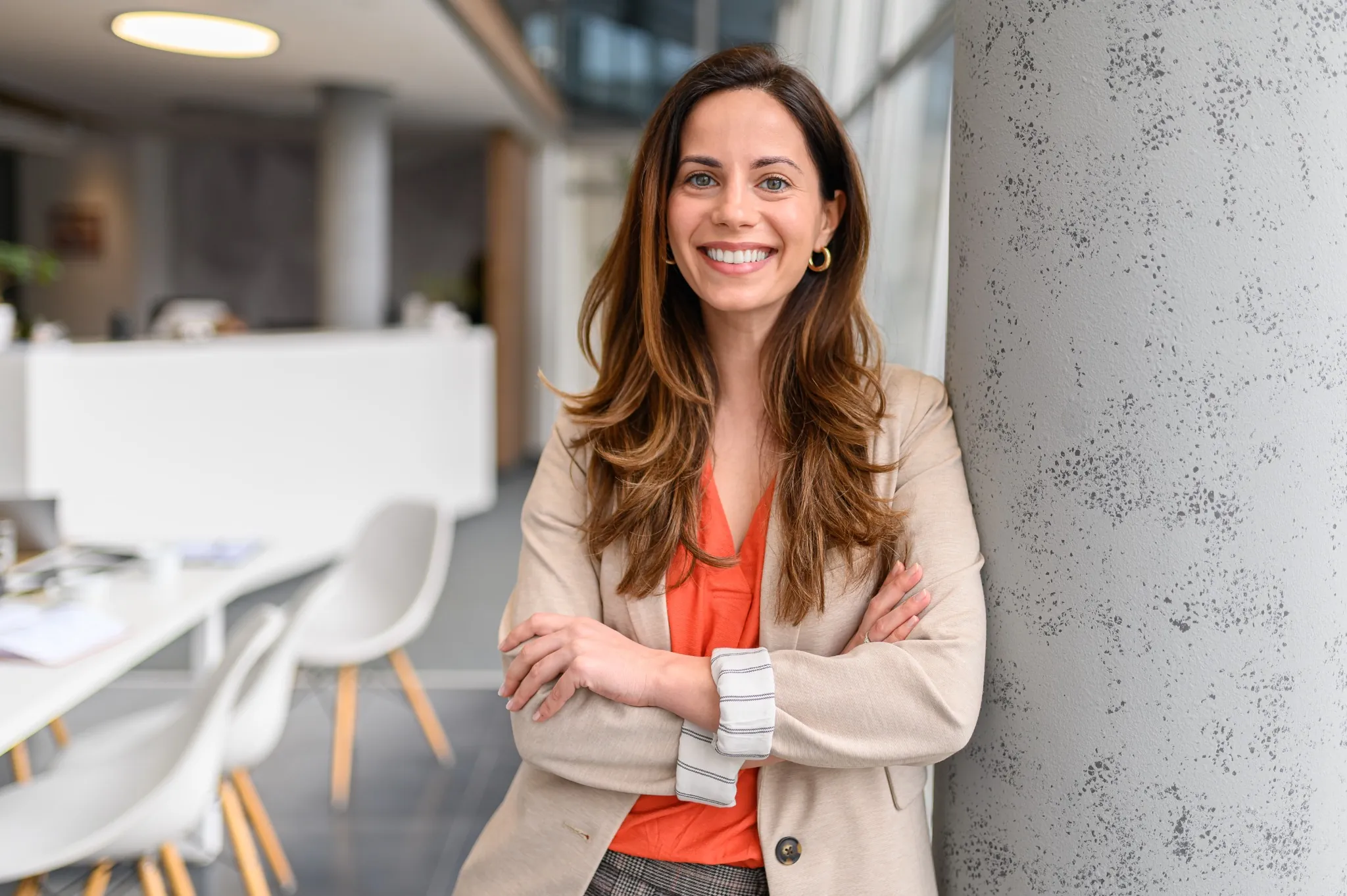 Business woman smiling with crossed arms leaning against pillar in workplace
