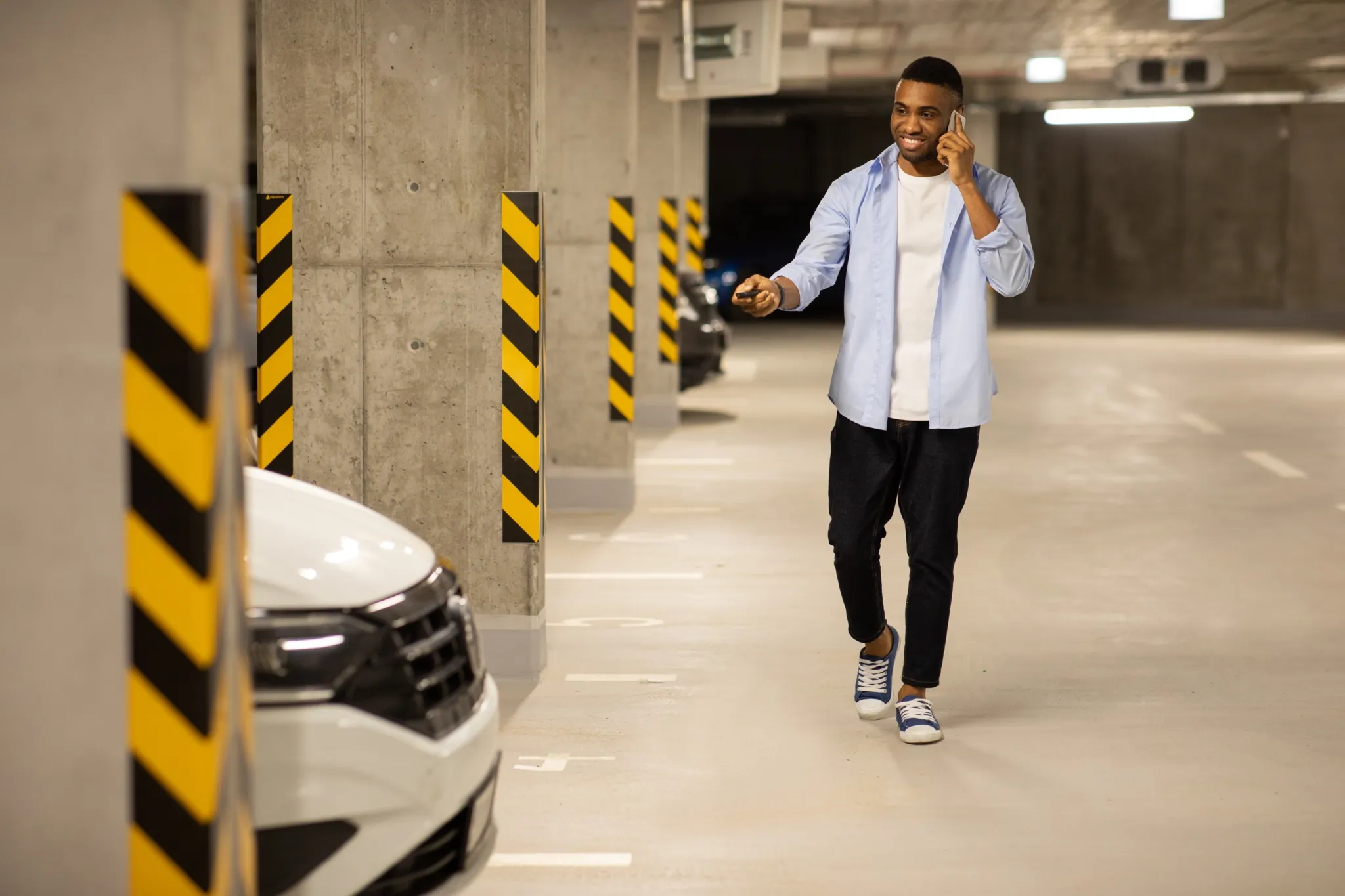 African american man opens his car with keys in an underground parking lot while talking on the phone