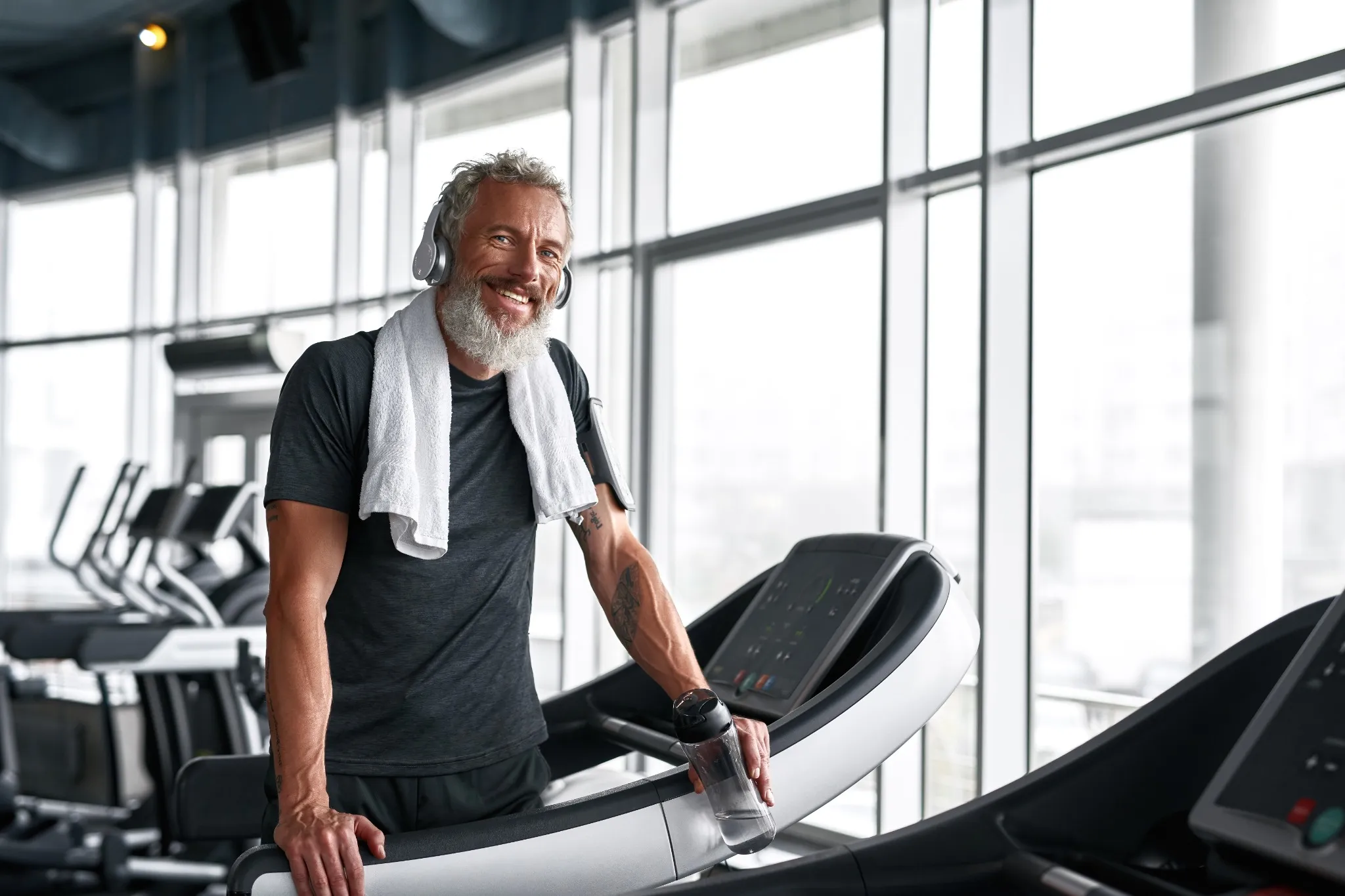 Cheerful grey-haired man with towel around neck, posing in gym.