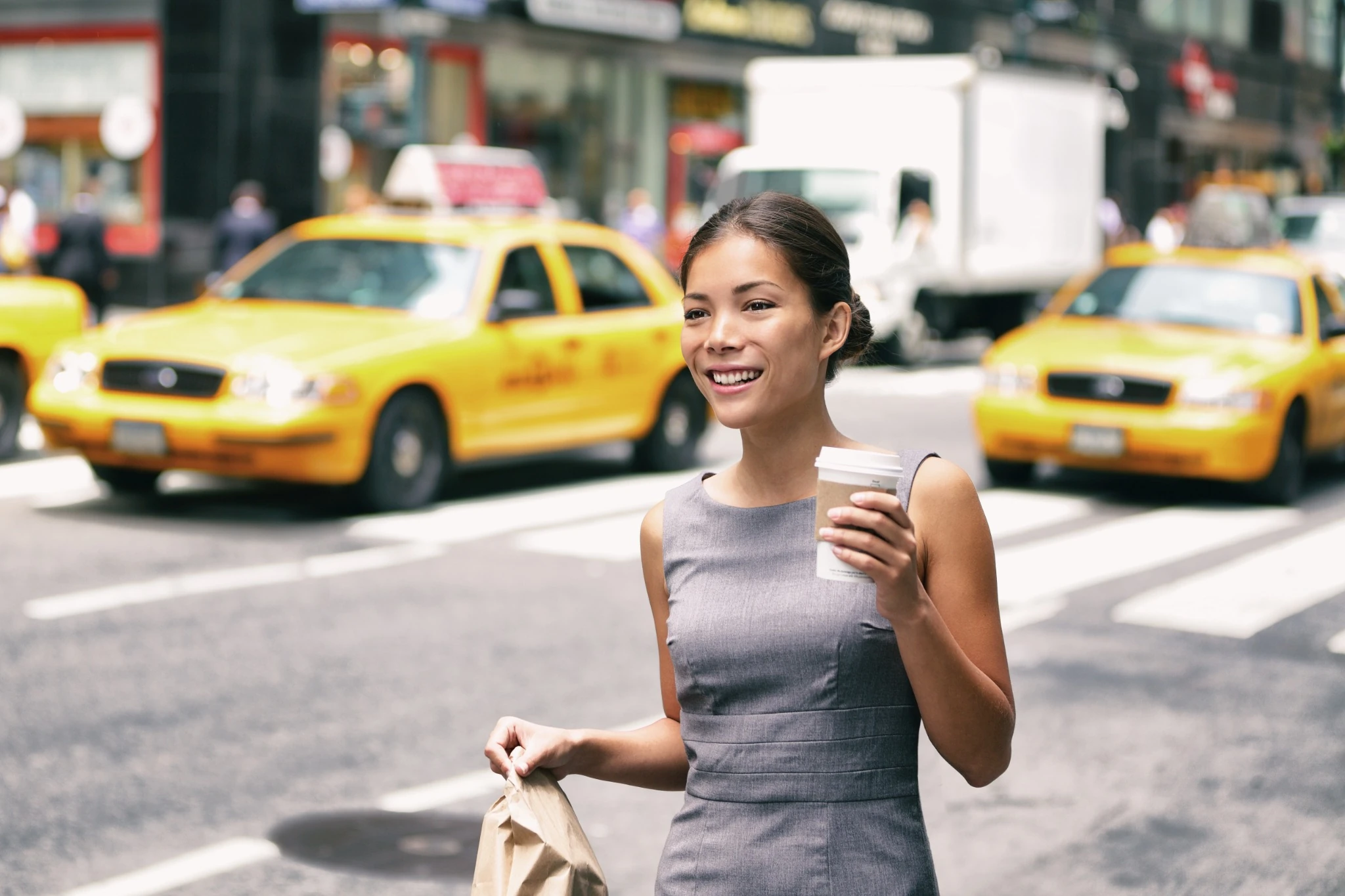 asian business woman with a coffee walking in front of taxi cabs on nyc street