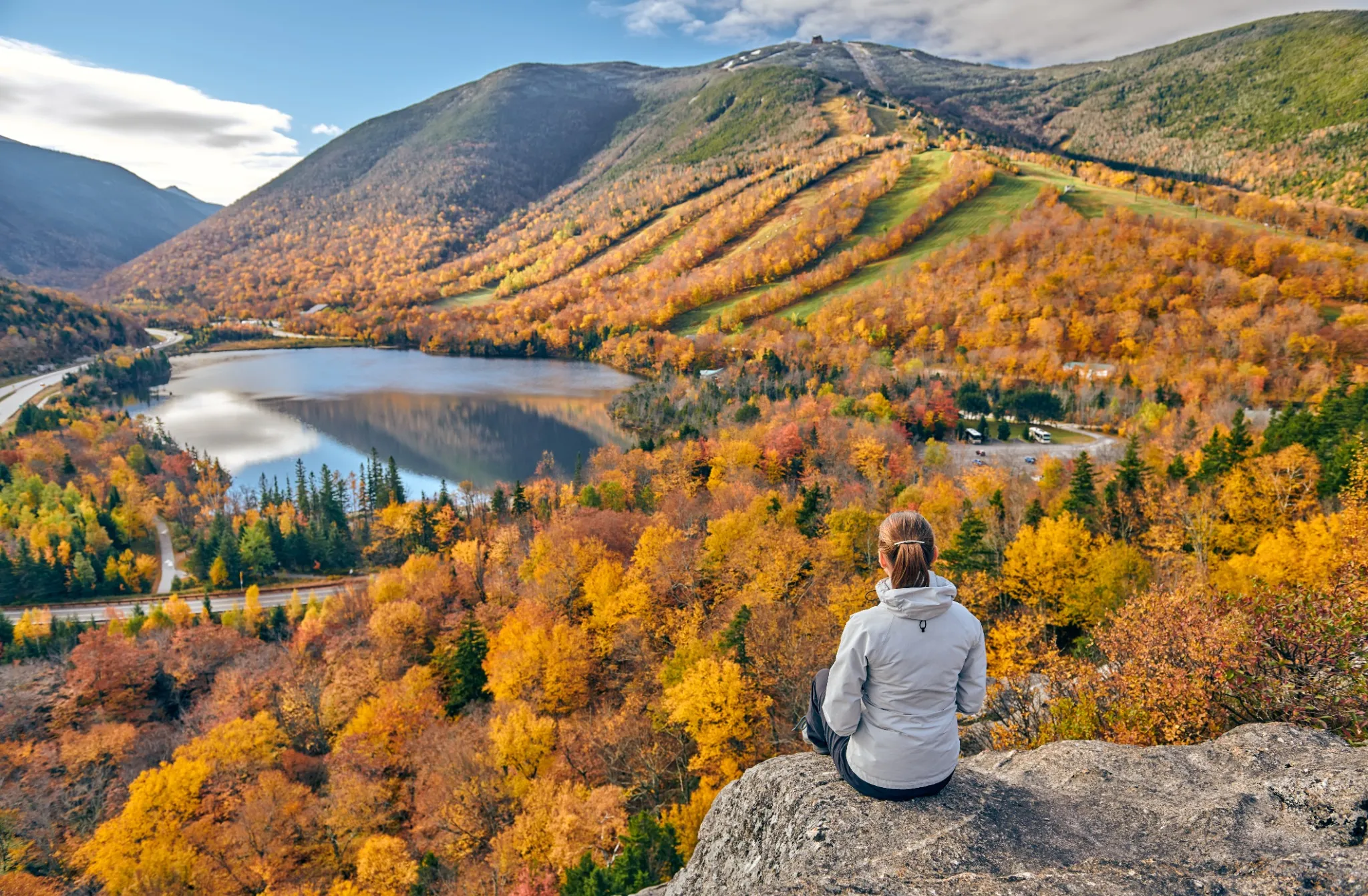 Woman hiking at Artist's Bluff in autumn. View of Echo Lake. Fall colours in Franconia Notch State Park. White Mountain National Forest,