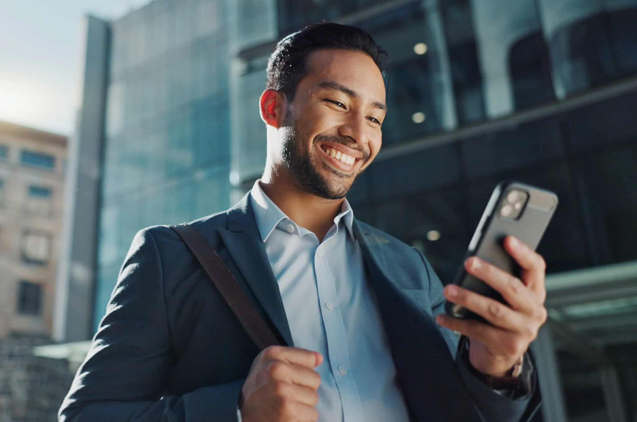 Man wearing a business suit smiling at his phone with high rise buildings in the background