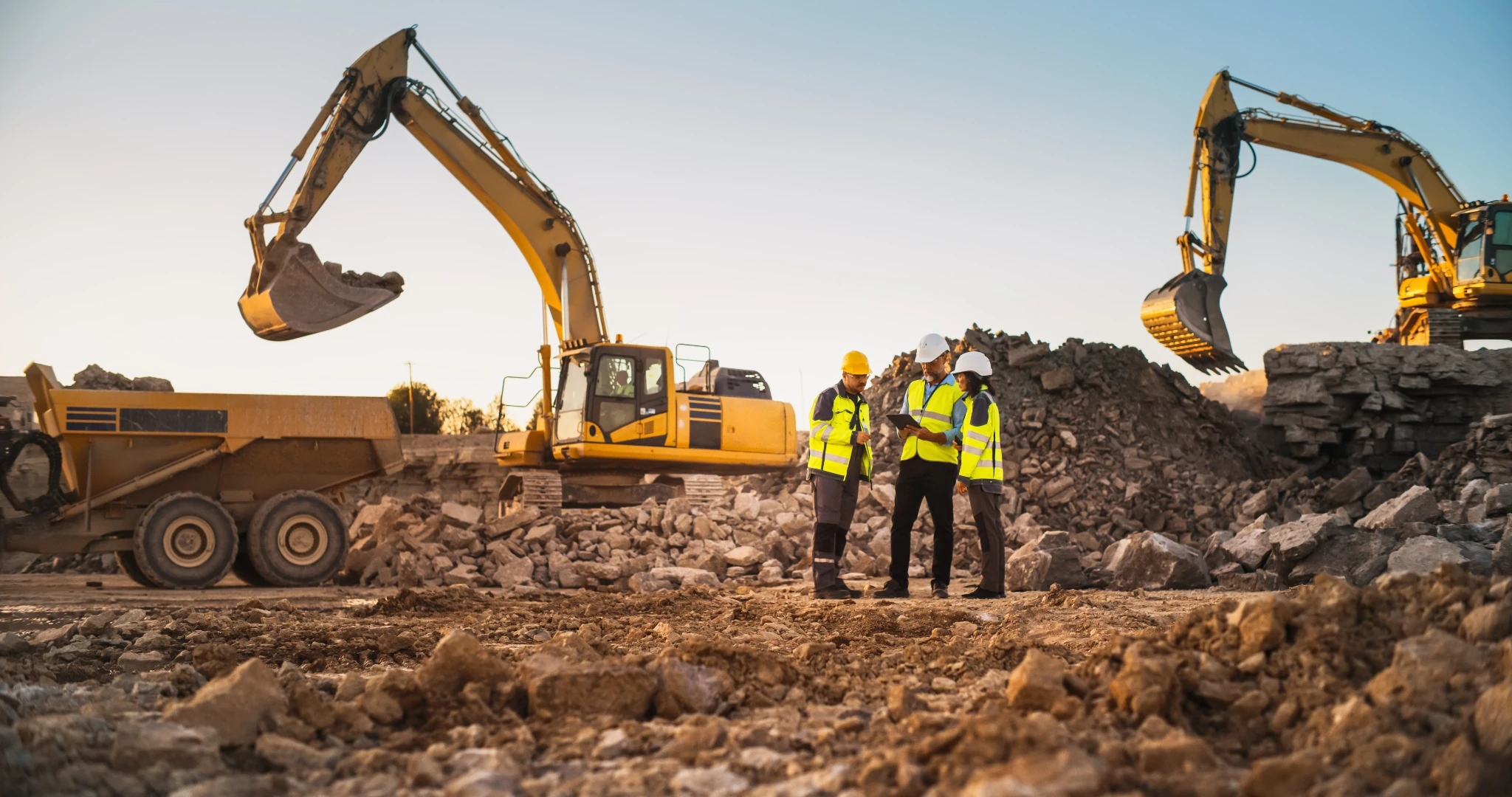 Construction site with three workers and excavator near dirt pile