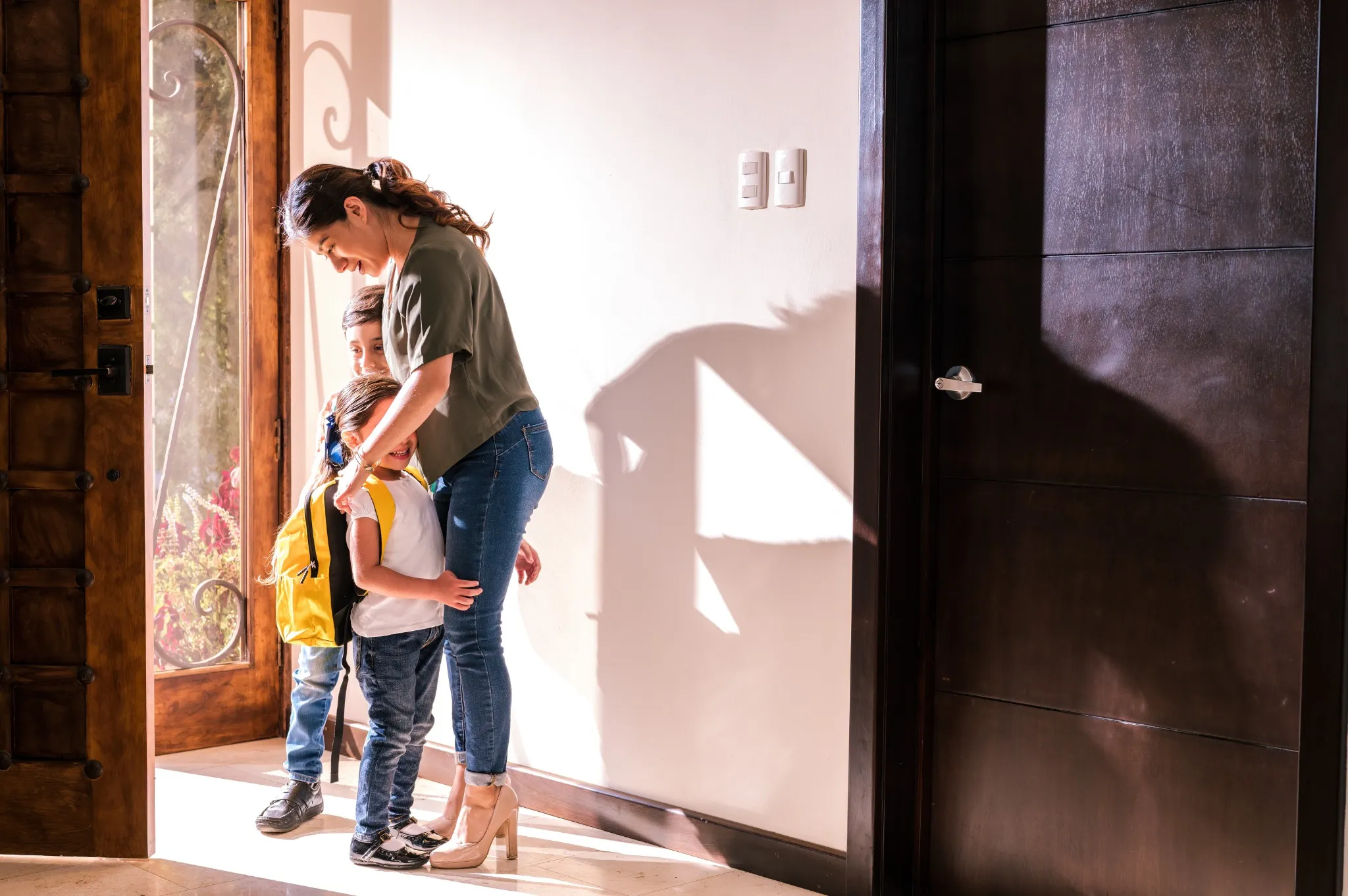 Mother and her two children meet at the door of their home and the mother hugs them with love..