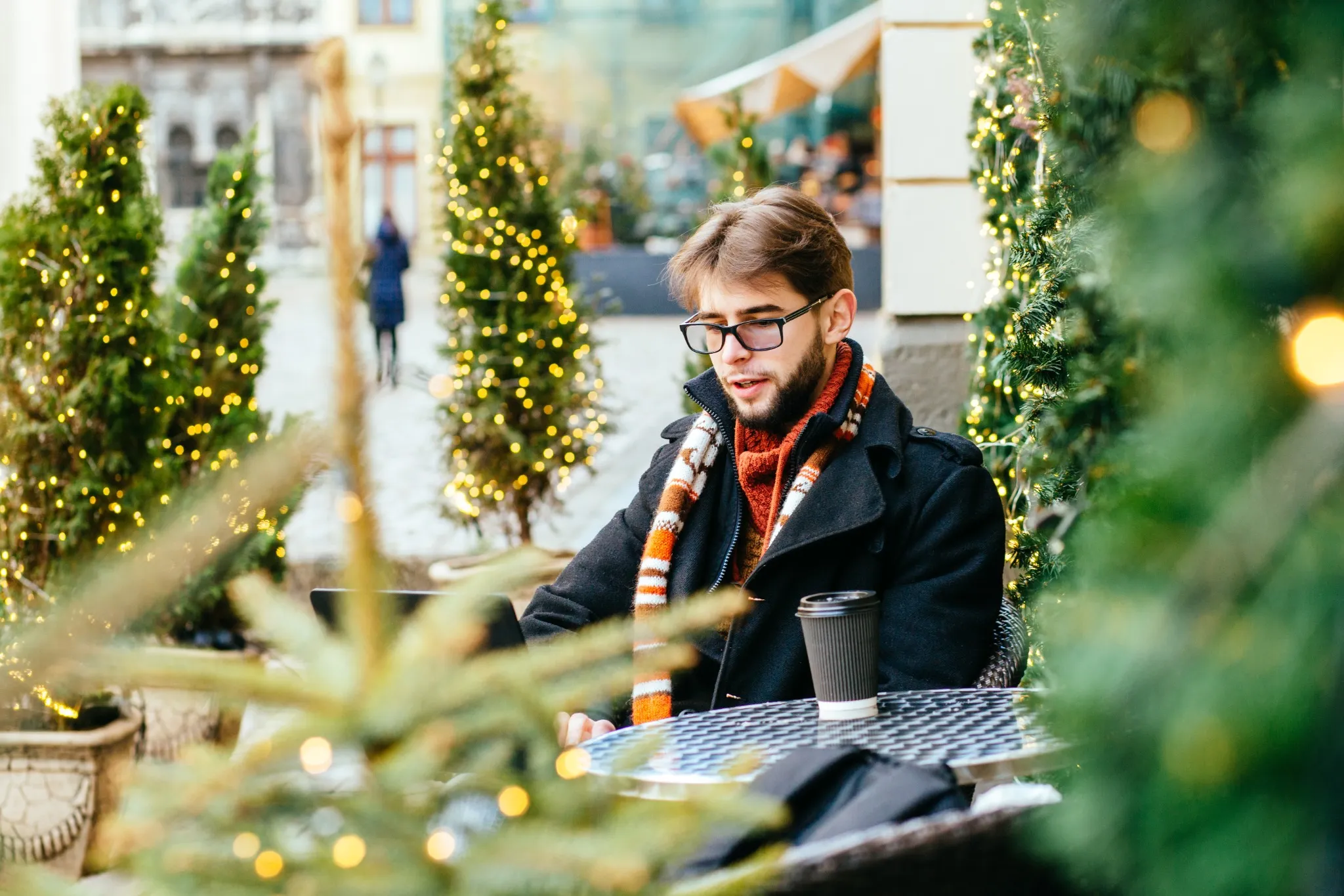 Handsome bearded man in glassessitting in cafe and working on laptop open air in winter time during sunny warm day..