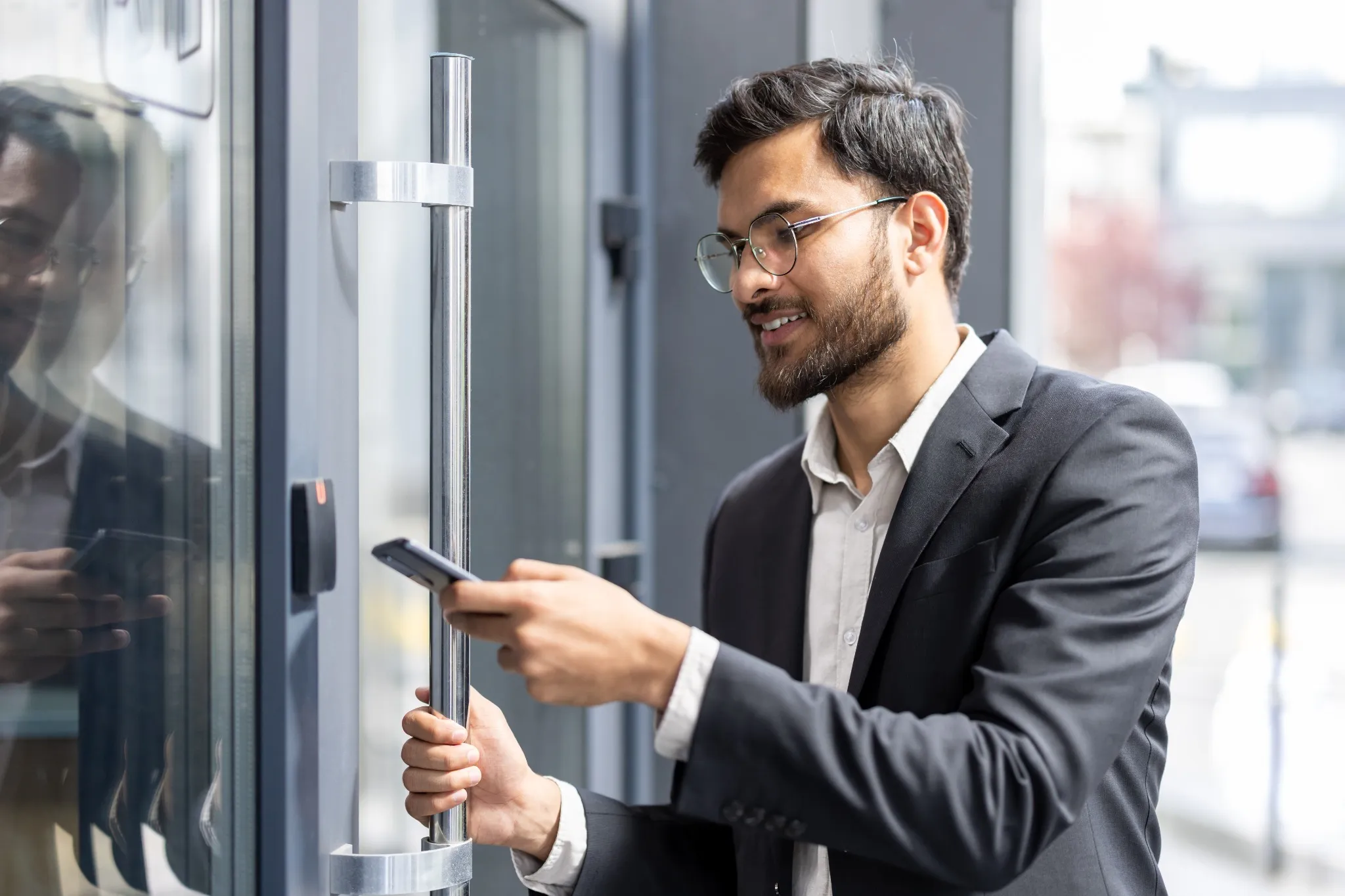 Indian businessman scanning smartphone at office entrance to unlock door with nfc contactless access, showcasing secure, modern mobile authentication for corporate building access control.