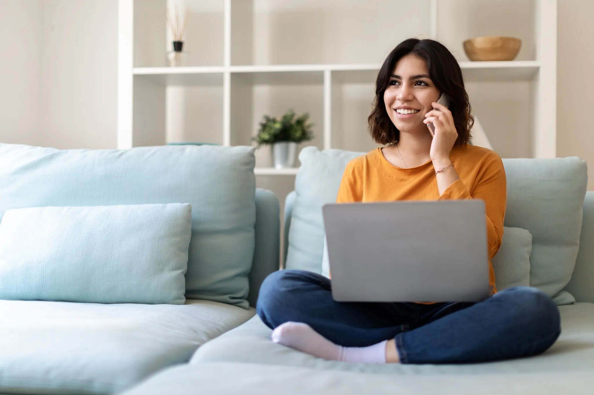 woman talking on phone sitting cross legged on couch with laptop