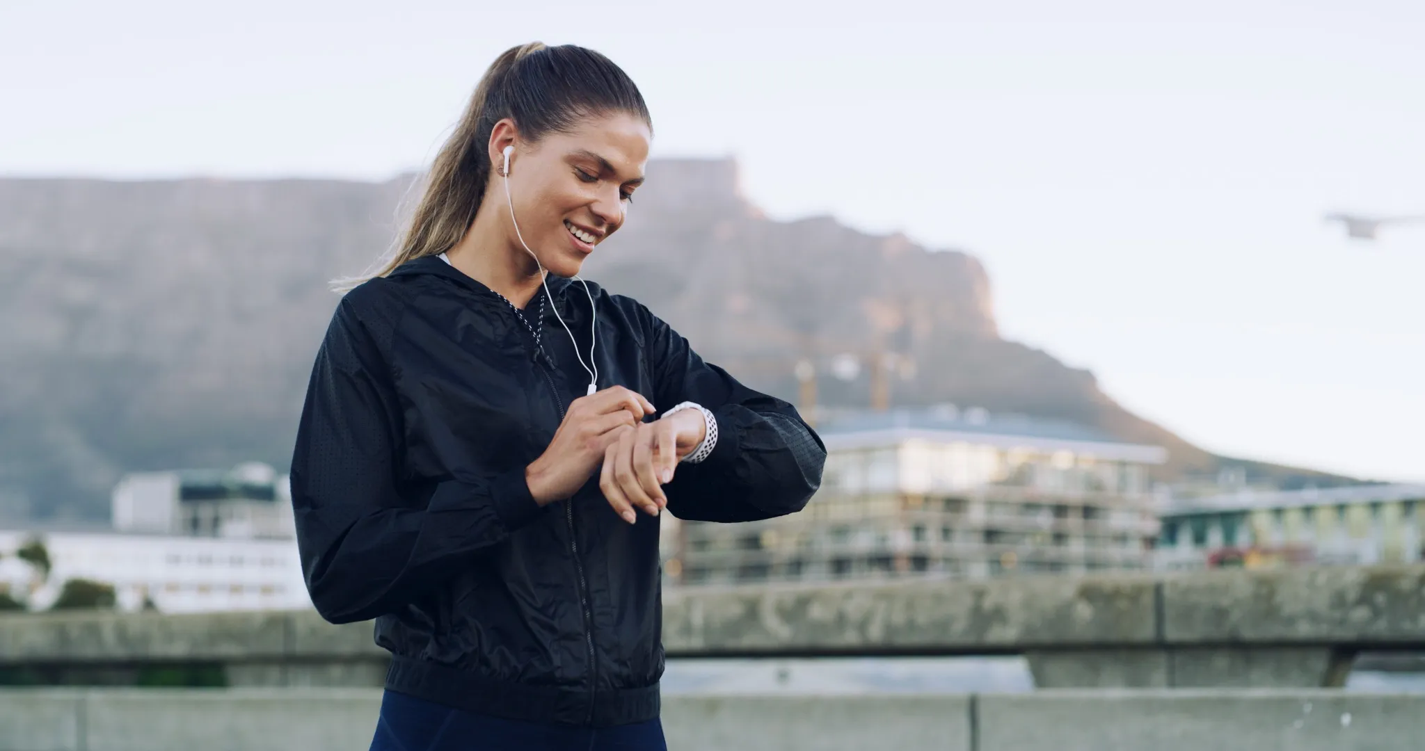 Woman, runner and smile with smart watch in city with timer, stats or earphones for music with fitness.