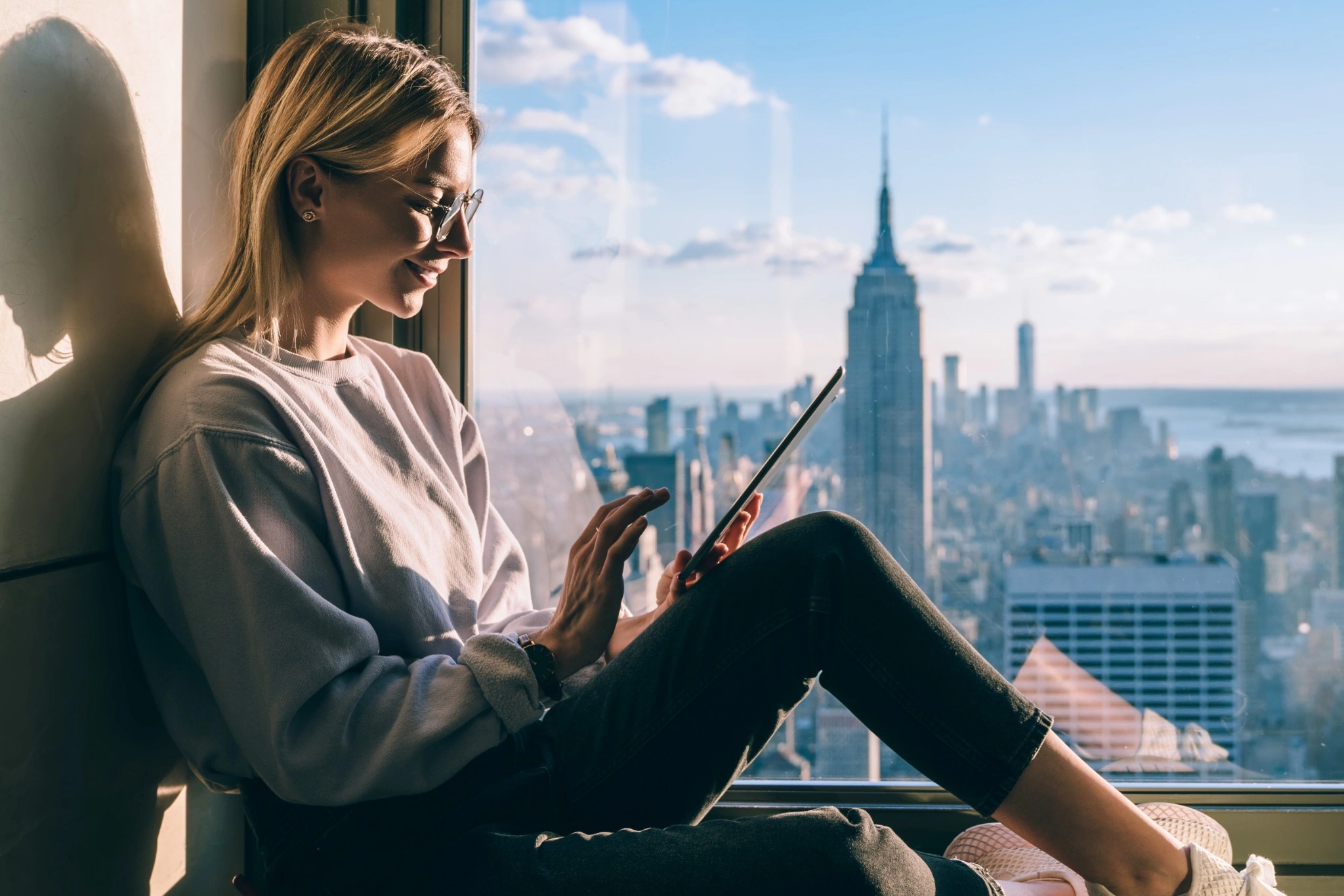 Young woman sitting in window sill on tablet with Manhattan in the background