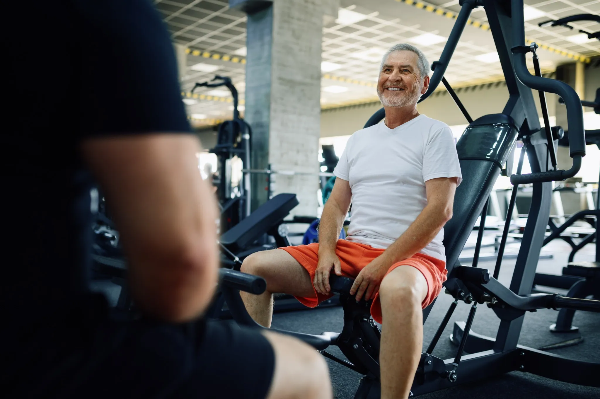 Elderly man poses on exercise machine in gym